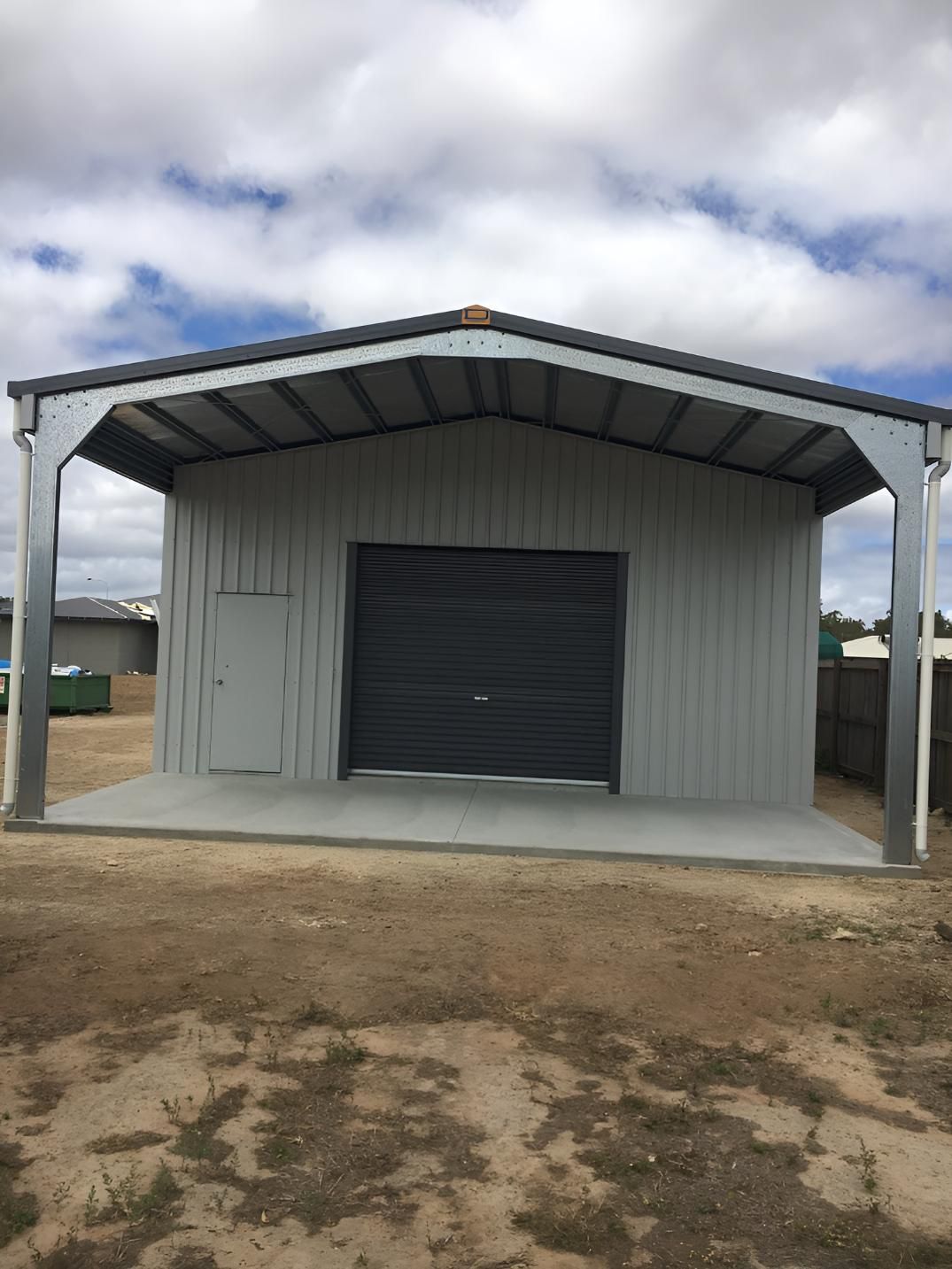 A Large Metal Building With A Black Garage Door Is Sitting In The Middle Of A Dirt Field — Dunnrite Mareeba Sheds & Garages In Atherton, QLD