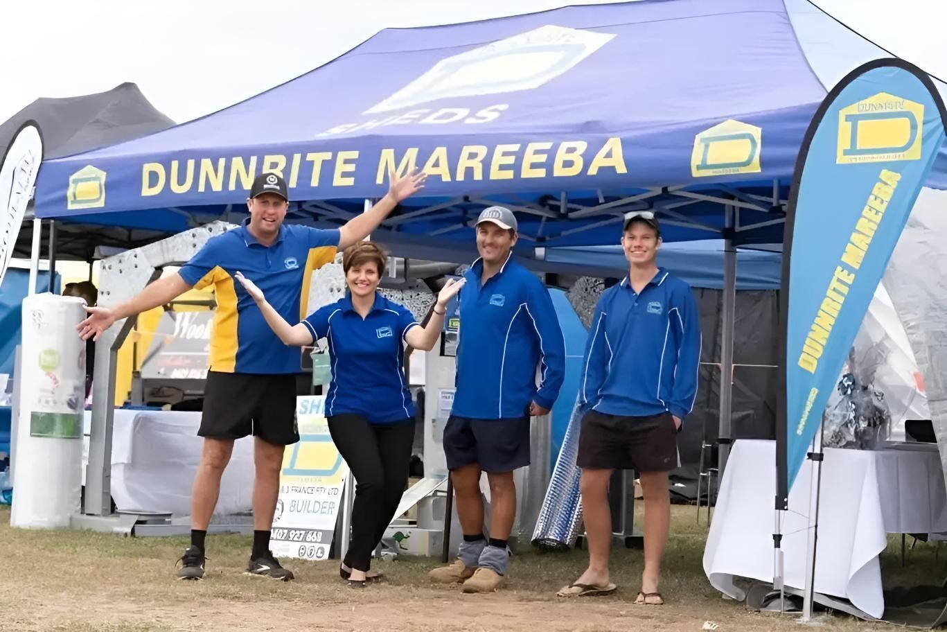 A Group Of People Standing Under A Blue Dunnrite Mareeba Tent — Dunnrite Mareeba Sheds & Garages In Mareeba, QLD