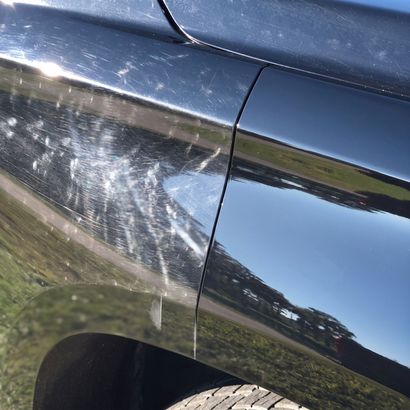 Close-up of a black car door and fender with white scuff marks and scratches
