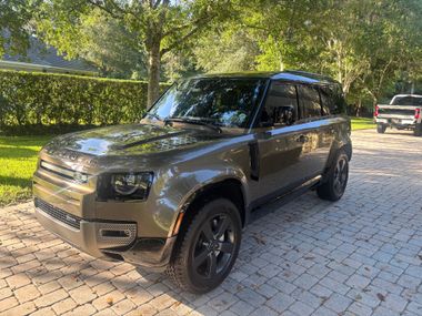Bronze SUV parked on a cobblestone driveway under trees, with another vehicle in the background.