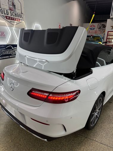 White convertible sports car with roof panel raised indoors, showing rear lights and gray interior.