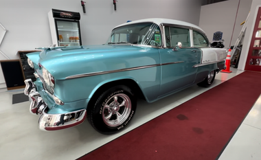 Turquoise vintage car with white roof displayed indoors on a red carpet
