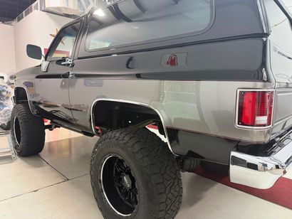 Lifted silver pickup truck with black canopy and oversized off-road tires in a garage
