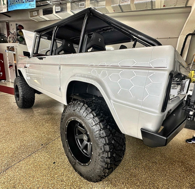 White lifted off-road truck with black roll cage and oversized tires in a showroom