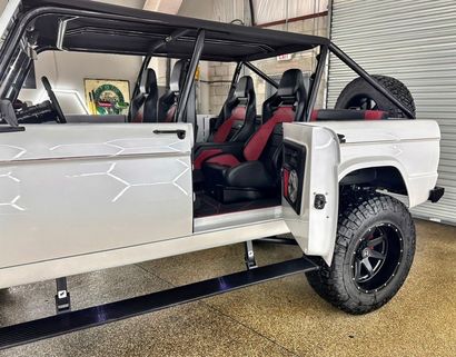 White off-road SUV with open door, black roll cage, and red seats inside a showroom.