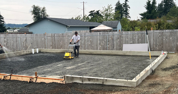 Worker compacting a gravel base inside concrete forms before a pour