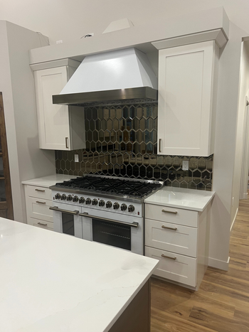 Kitchen remodel featuring white cabinets, a stainless steel range hood, and a dark tile backsplash