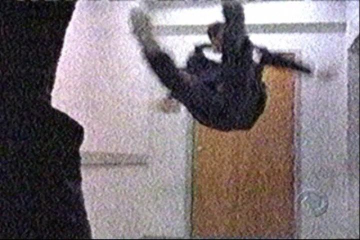 A person in dark clothing performs an aerial martial arts kick inside a room with a wooden door.
