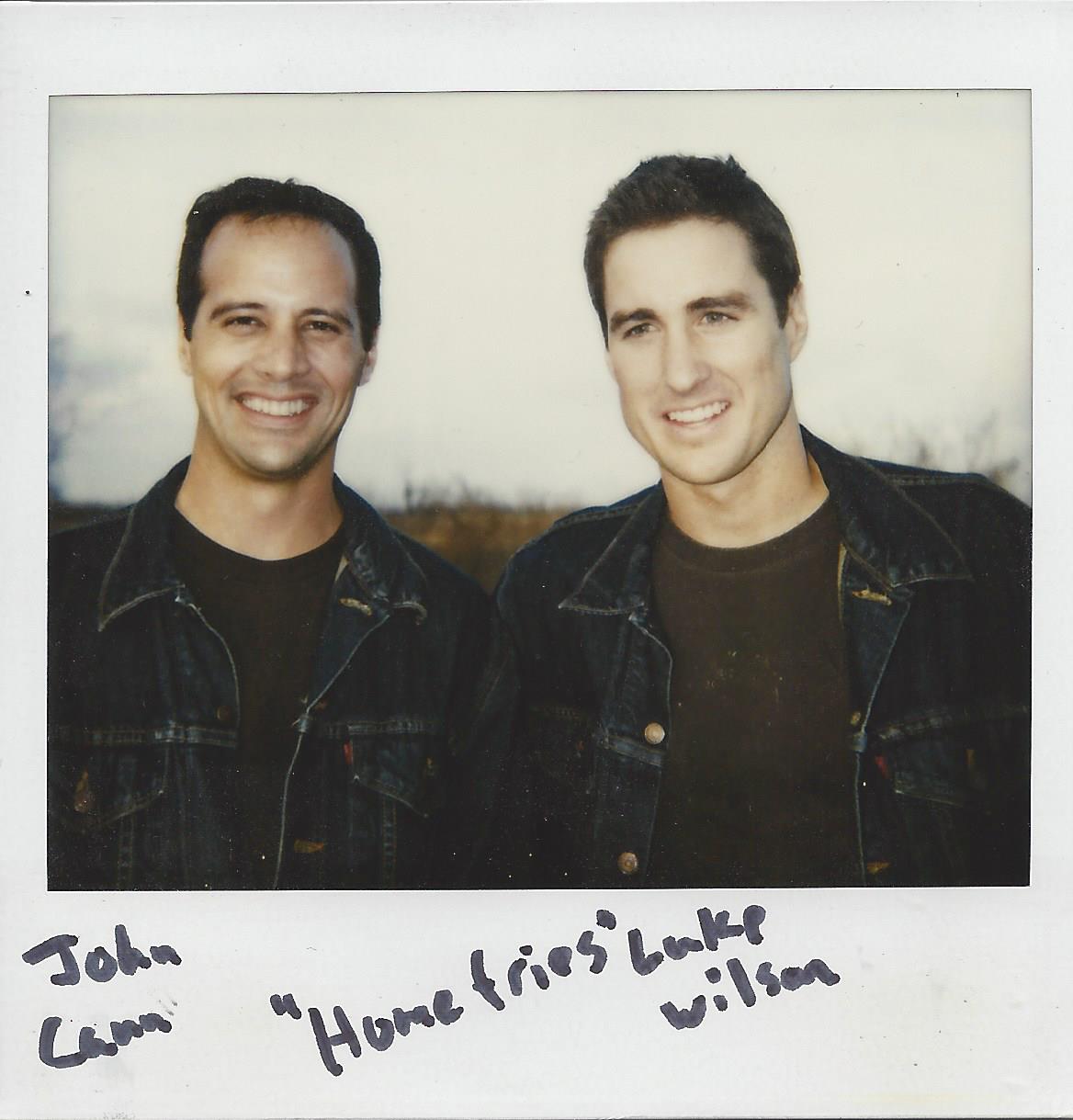 Polaroid of John Camm and Luke Wilson smiling while wearing dark jackets, with the text 