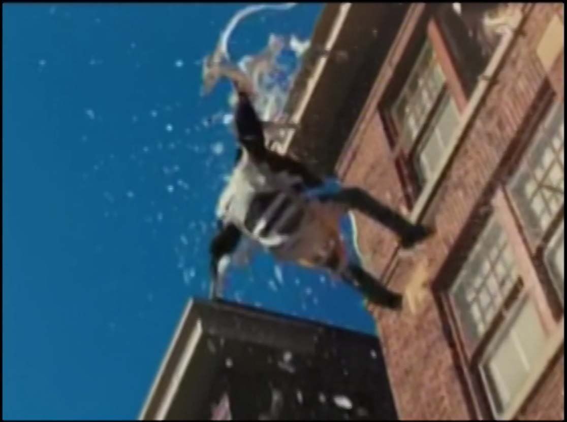 A person in a black-and-white outfit leaps from a building rooftop against a bright blue sky amidst falling debris.