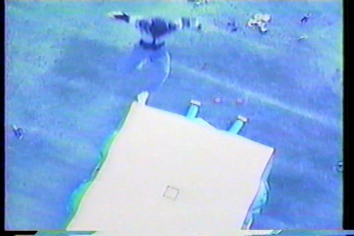 A person suspended in the air above a white crash mat, likely during a jump or fall in a training or sport setting.