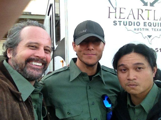 Three people in green shirts pose for a photo in front of a white 