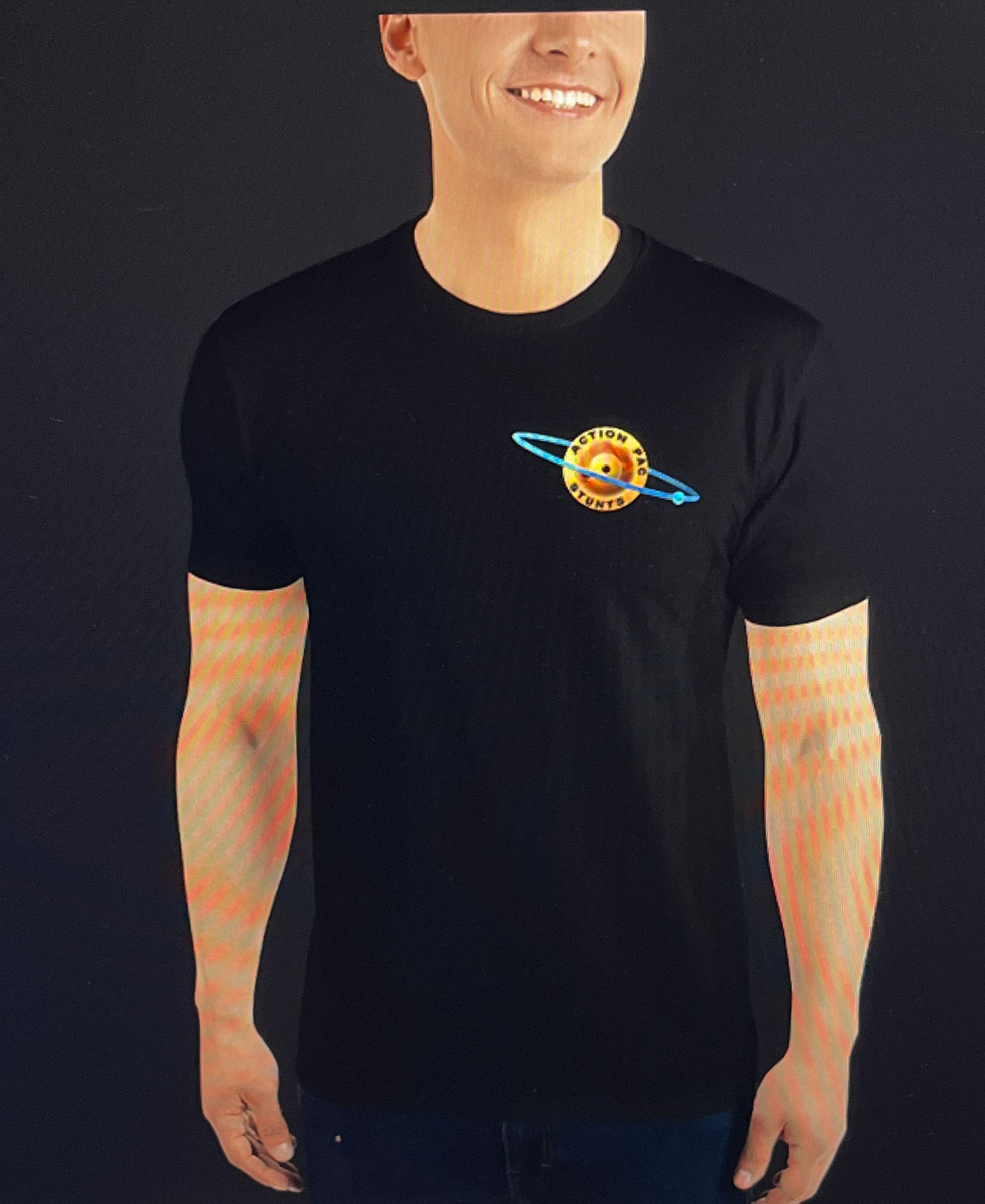 A smiling person wearing a black t-shirt featuring a small, circular yellow planet logo with a blue ring.