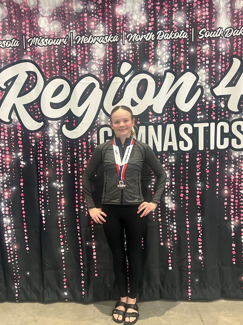 Person wearing a medal stands in front of a Region 4 Gymnastics backdrop.