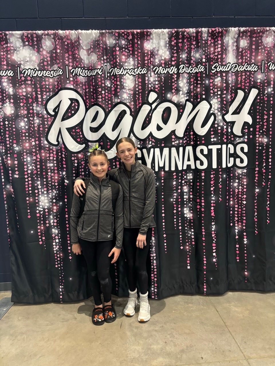 Two gymnasts posing in front of a “Region 4 Gymnastics” backdrop at an event