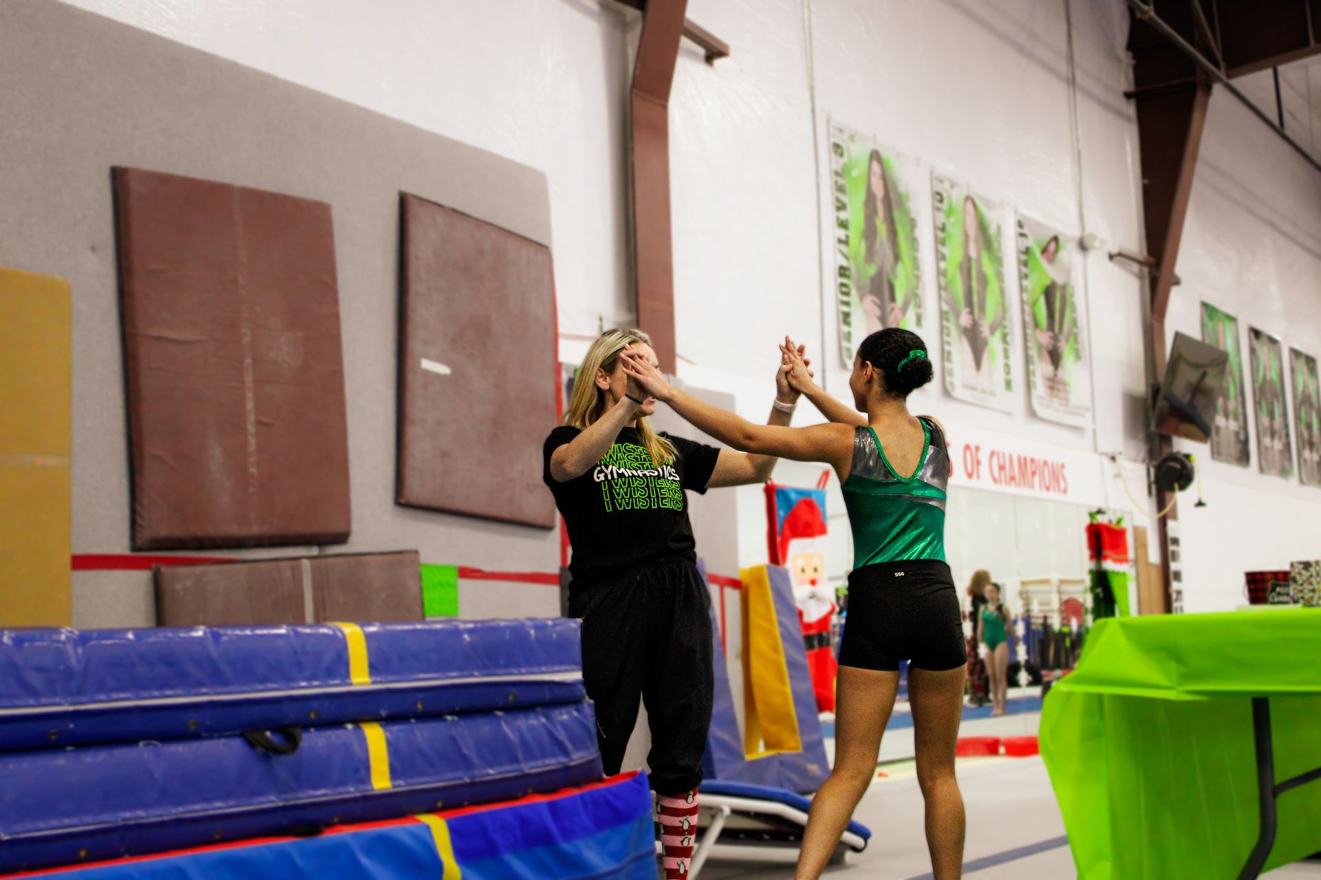 Two gymnasts spotting a handstand in a gym with mats and training equipment