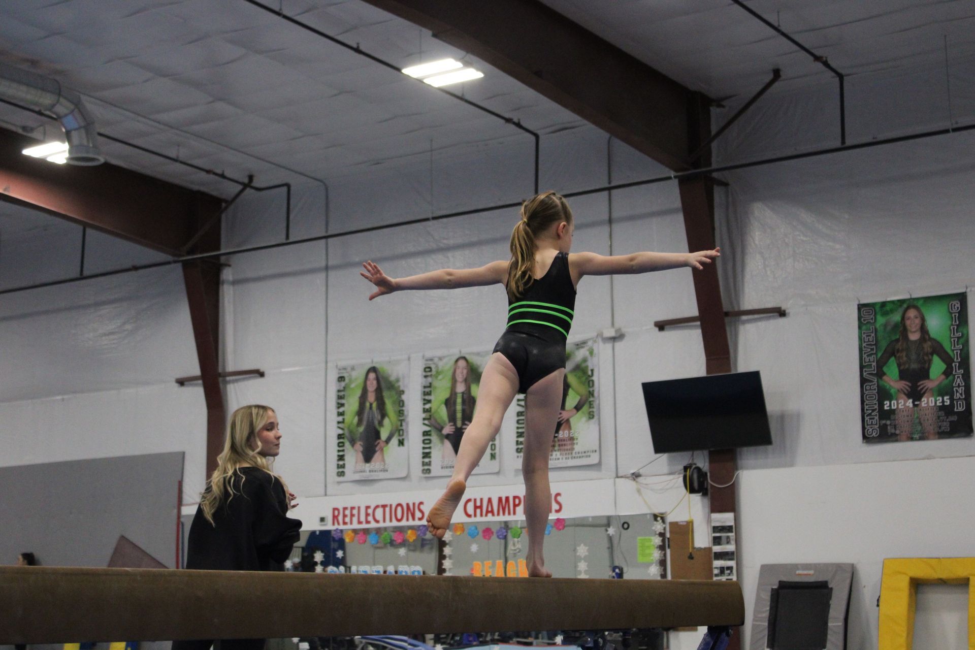 Gymnast balancing on a beam with arms outstretched in an indoor gym.