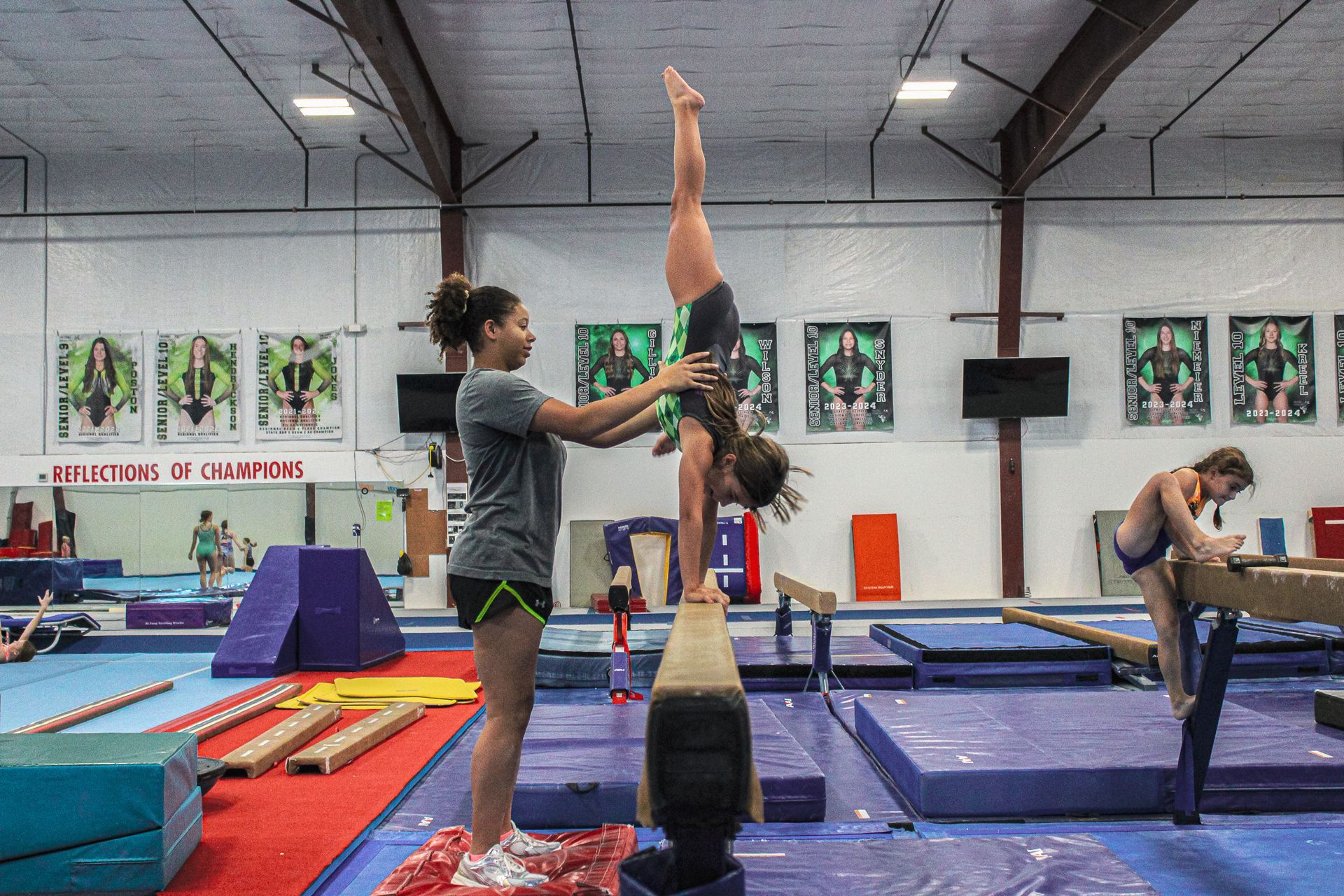 Gymnastics practice with two people spotting an upside-down gymnast on mats in a training gym