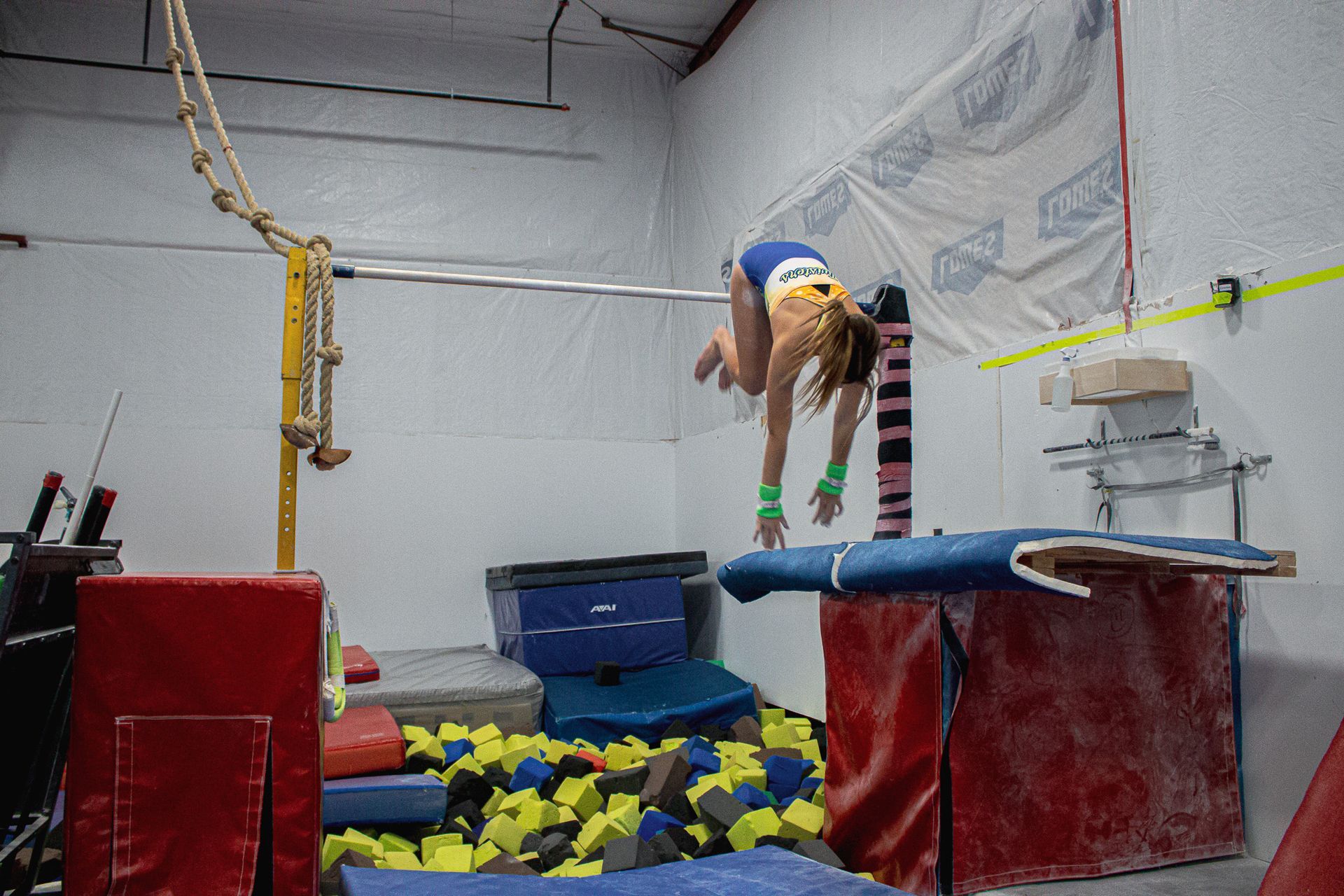 Gymnast mid-flip on a vault over a foam pit in an indoor training gym