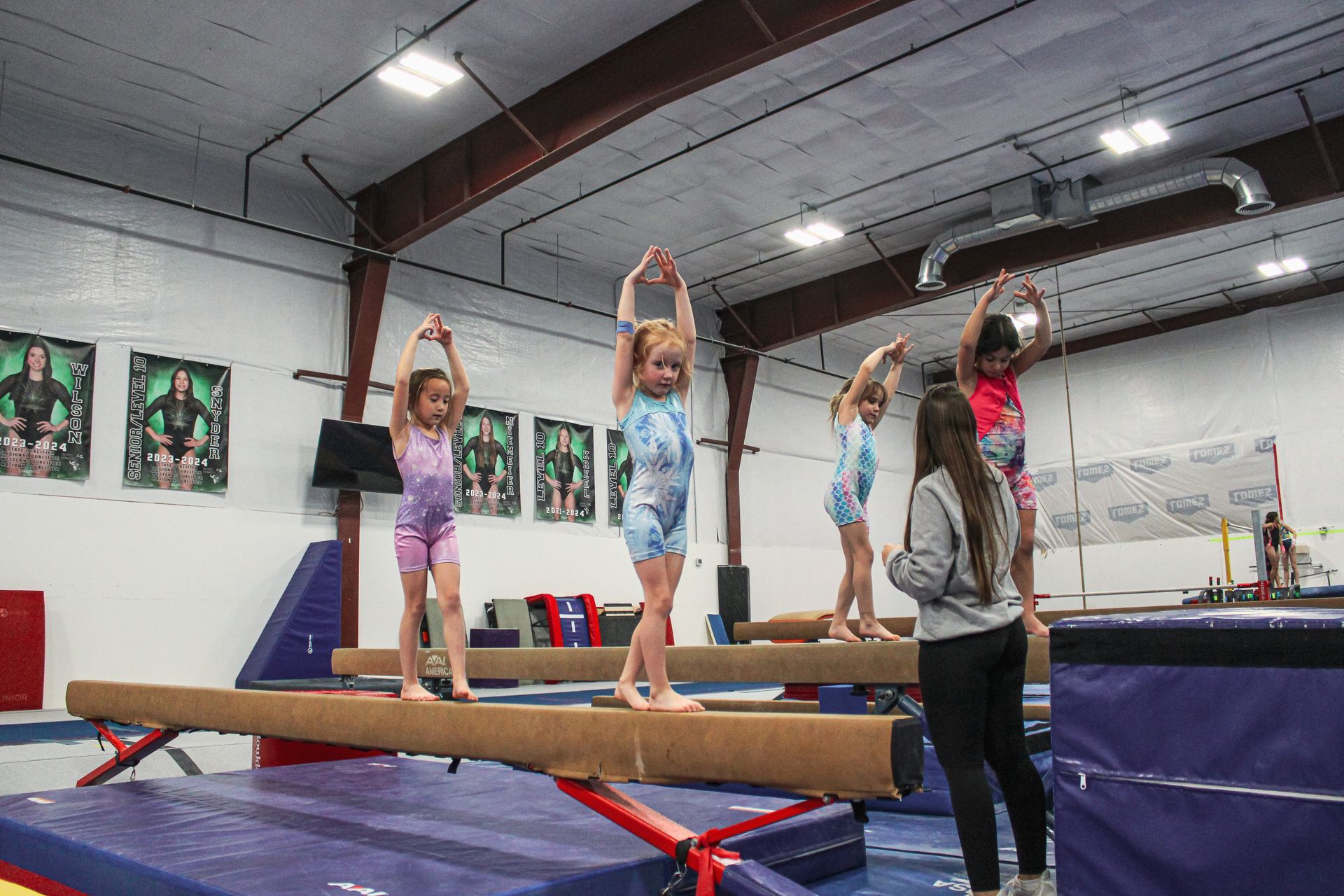 Gymnastics class with three children balancing on a beam in a gym, instructor nearby