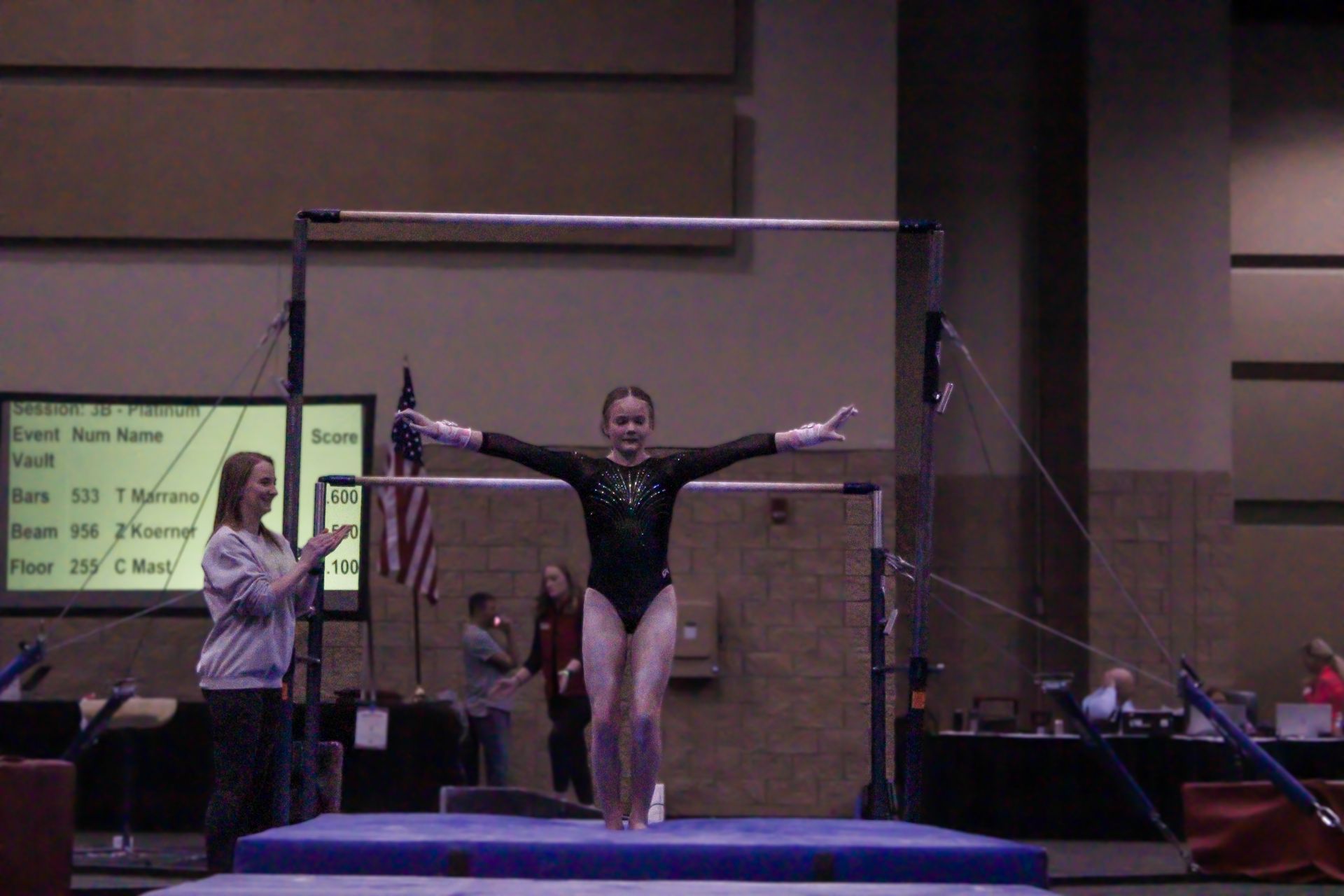 Gymnast on balance beam with arms outstretched in an indoor competition gym