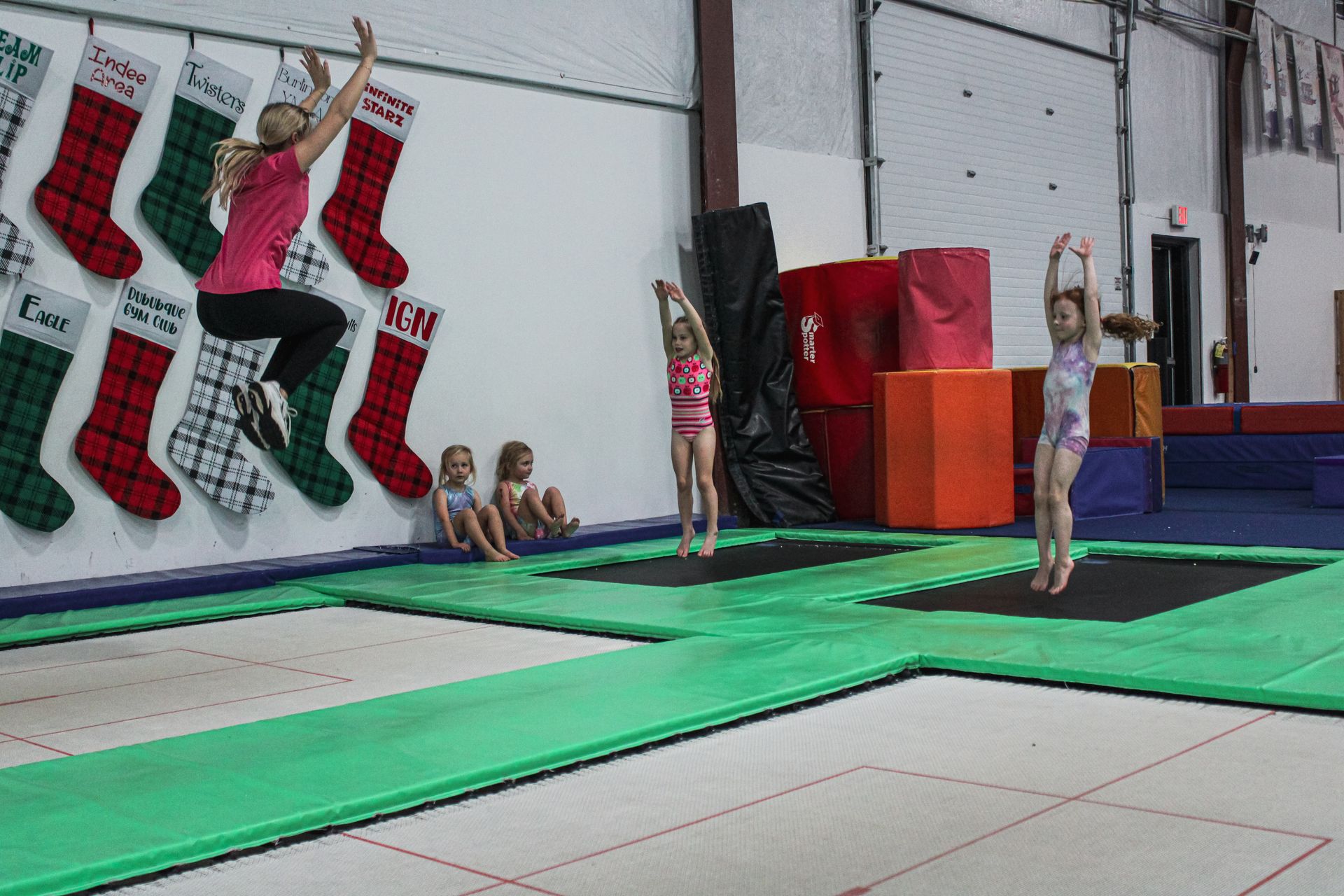 Gymnastics gym with children on trampolines and mats, practicing flips and handstands.