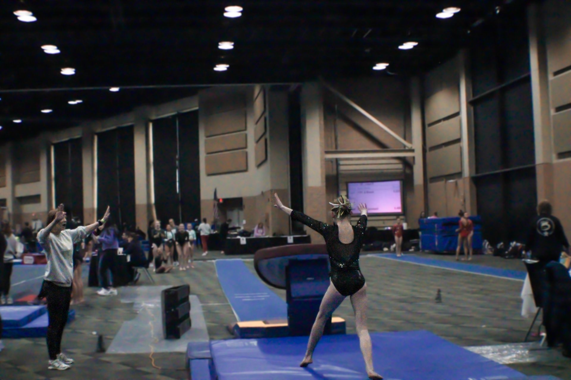 Indoor gymnastics floor routine with athletes on blue mats in a large convention hall