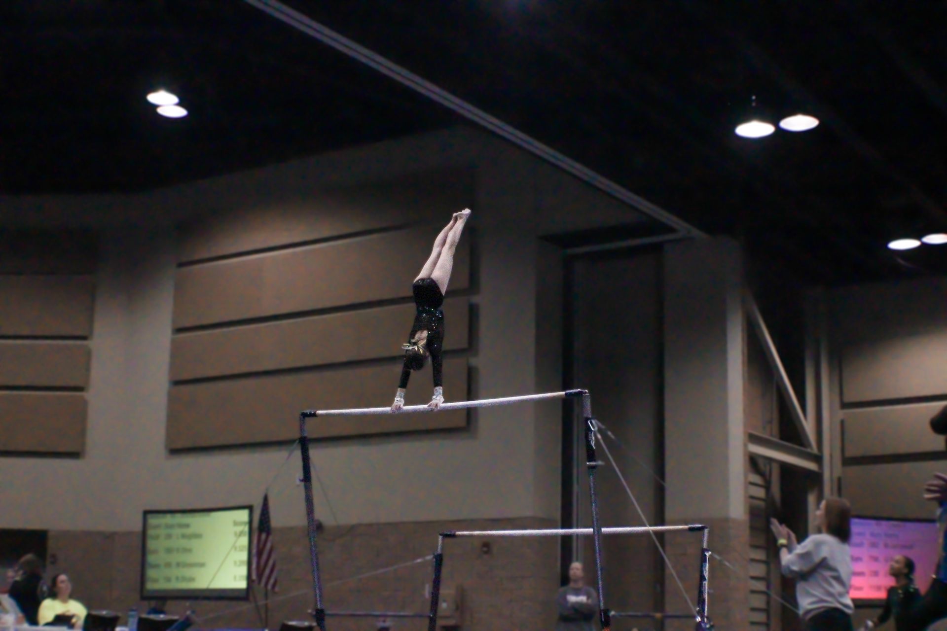 Gymnast balancing upside down on parallel bars in an indoor arena