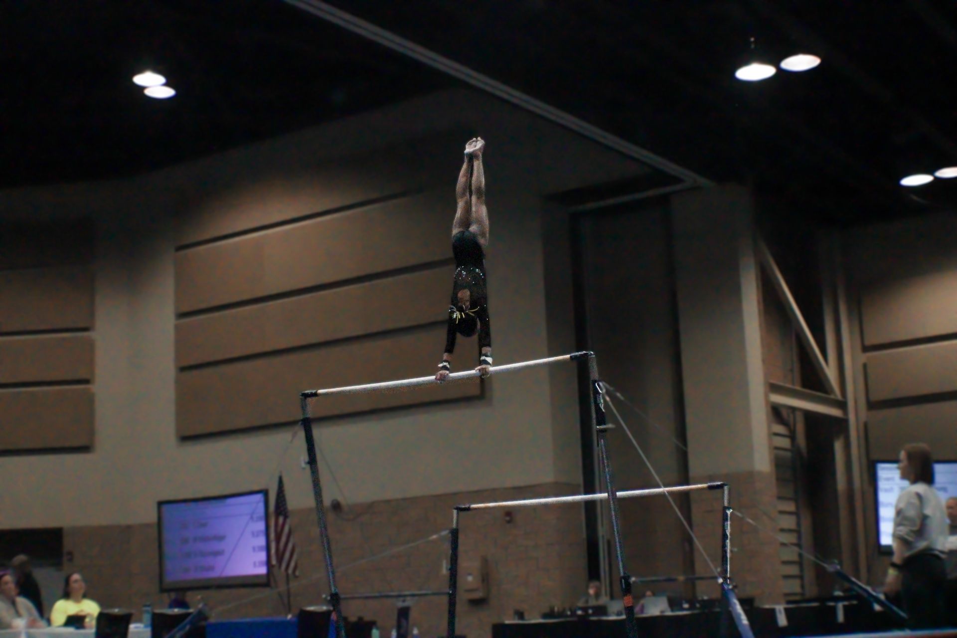 Gymnast balancing upside down on a high bar in an indoor arena