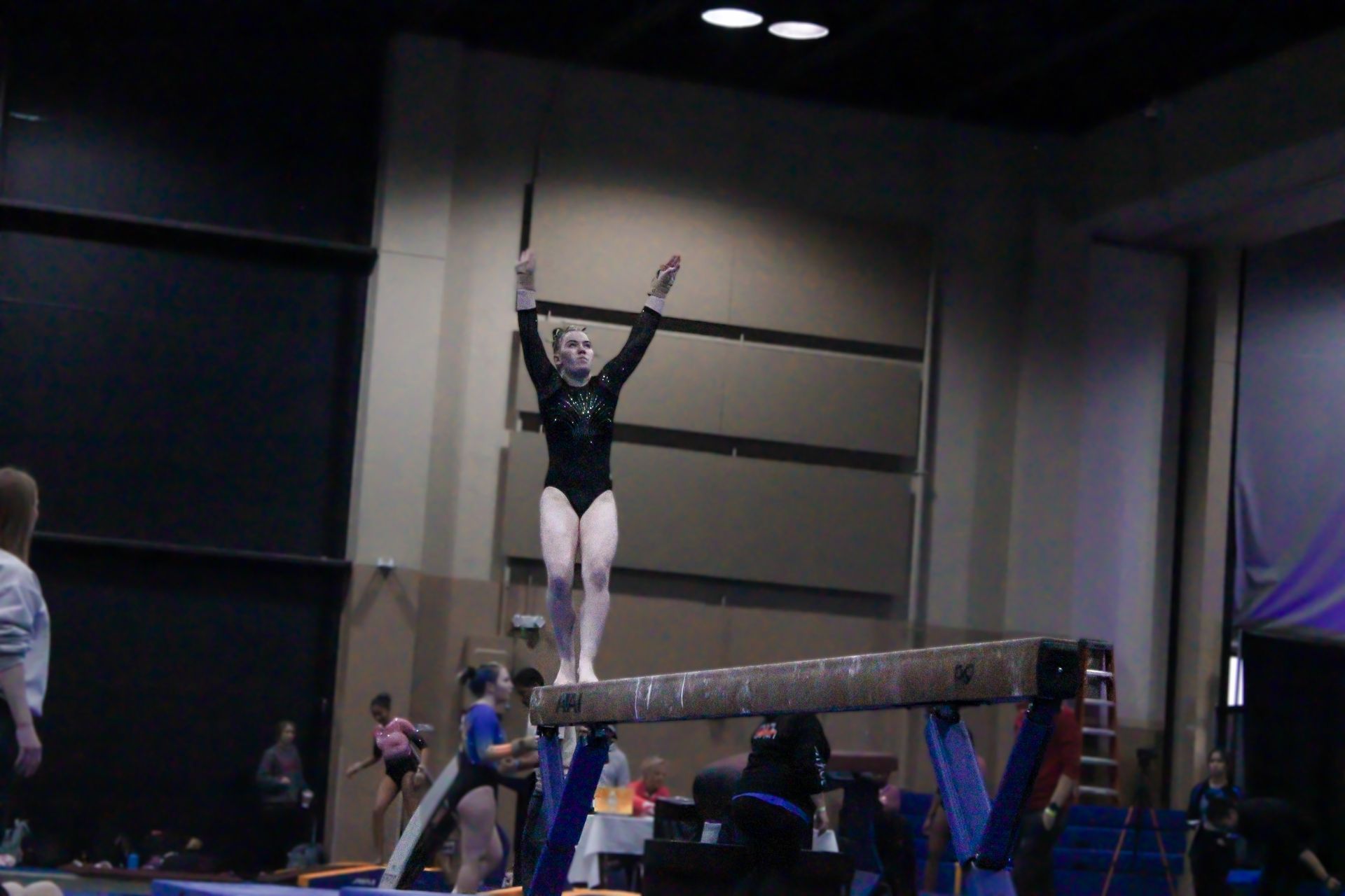 Gymnast in black leotard midair above the vault table during an indoor competition