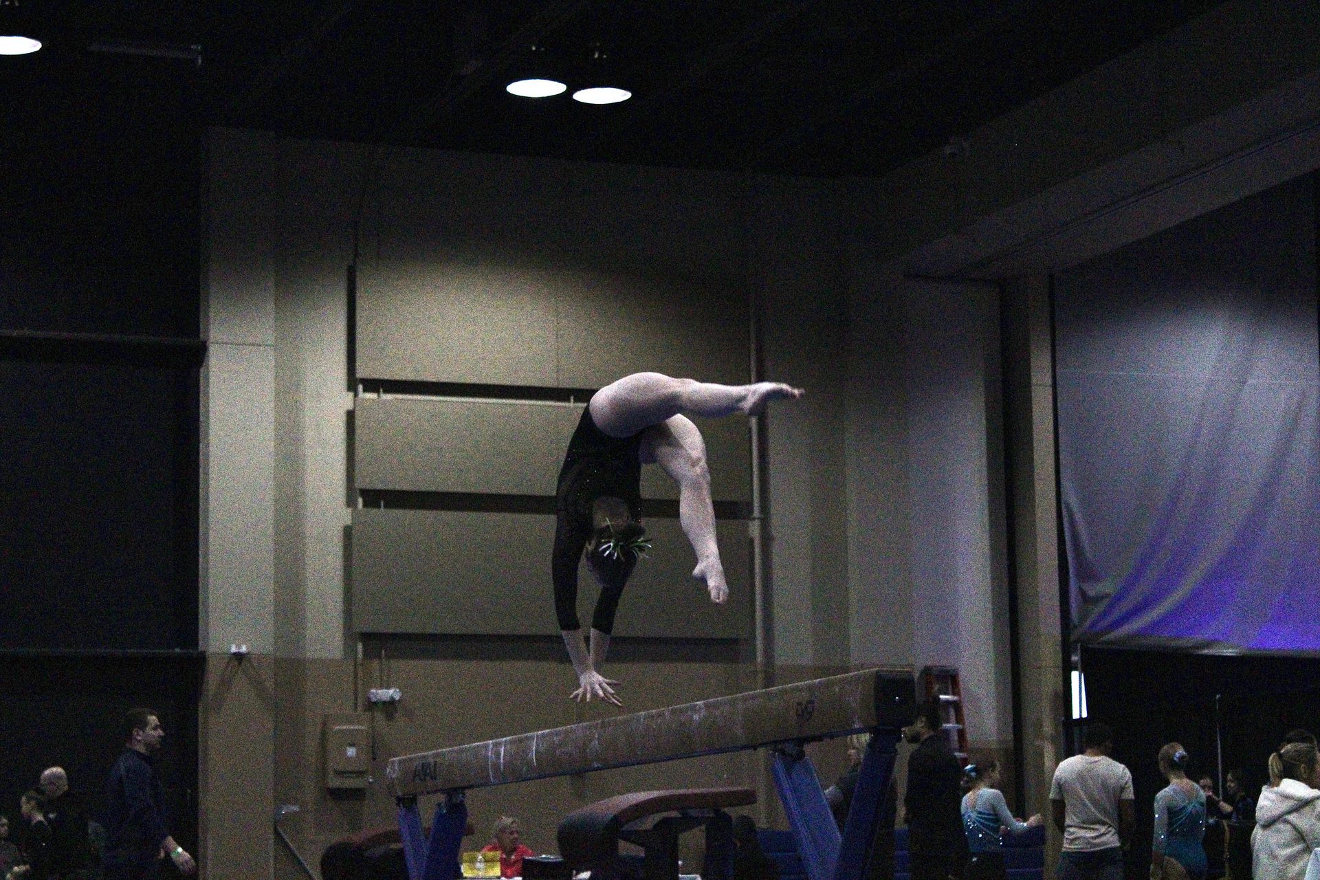 Gymnast mid-flip over a vault in an indoor competition arena