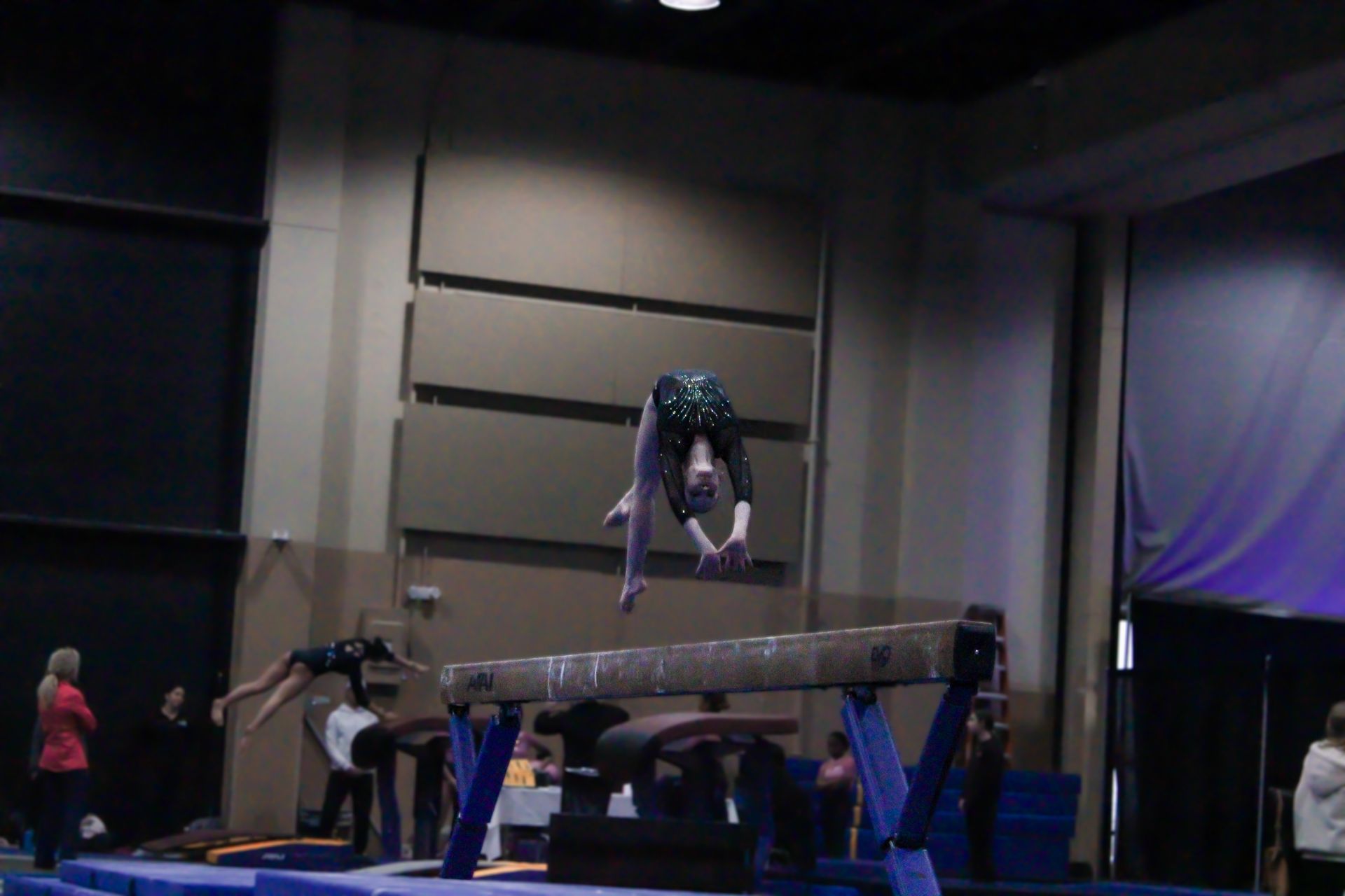 Gymnast upside down above a vault table in a dim indoor competition venue