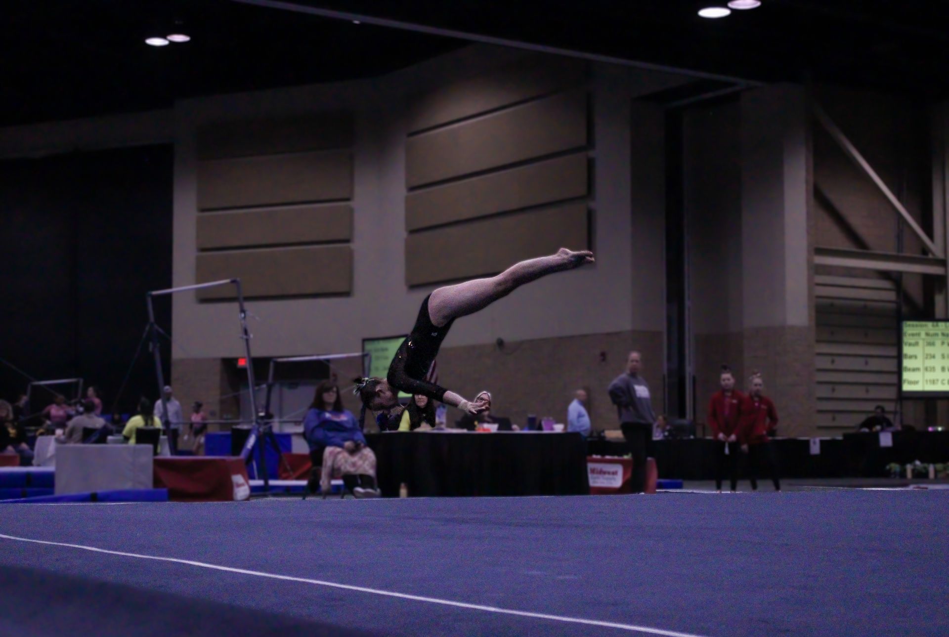 Gymnast performing a back handspring on a vault mat in an indoor sports arena