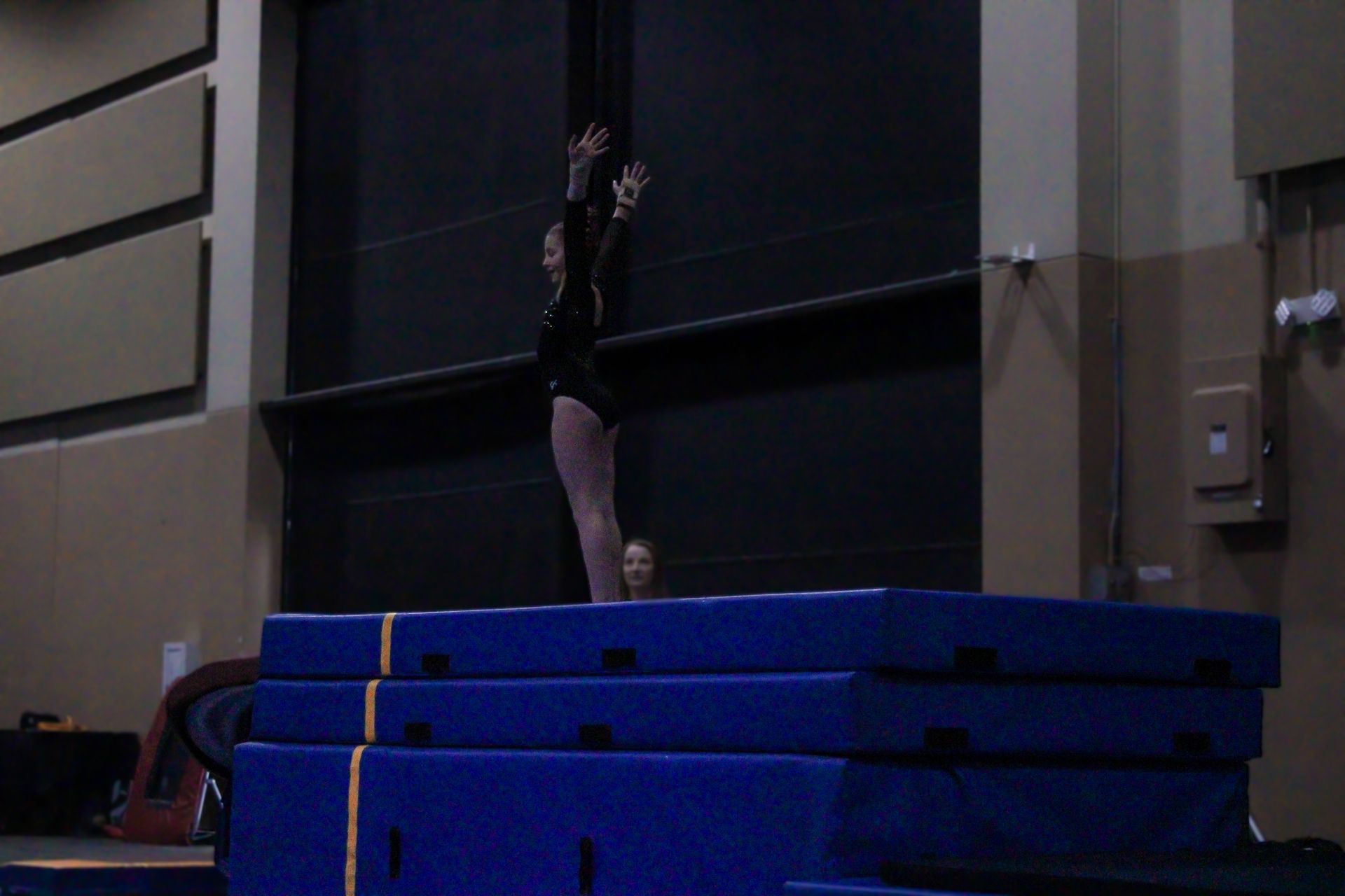 Gymnast balancing upside down on stacked blue mats indoors