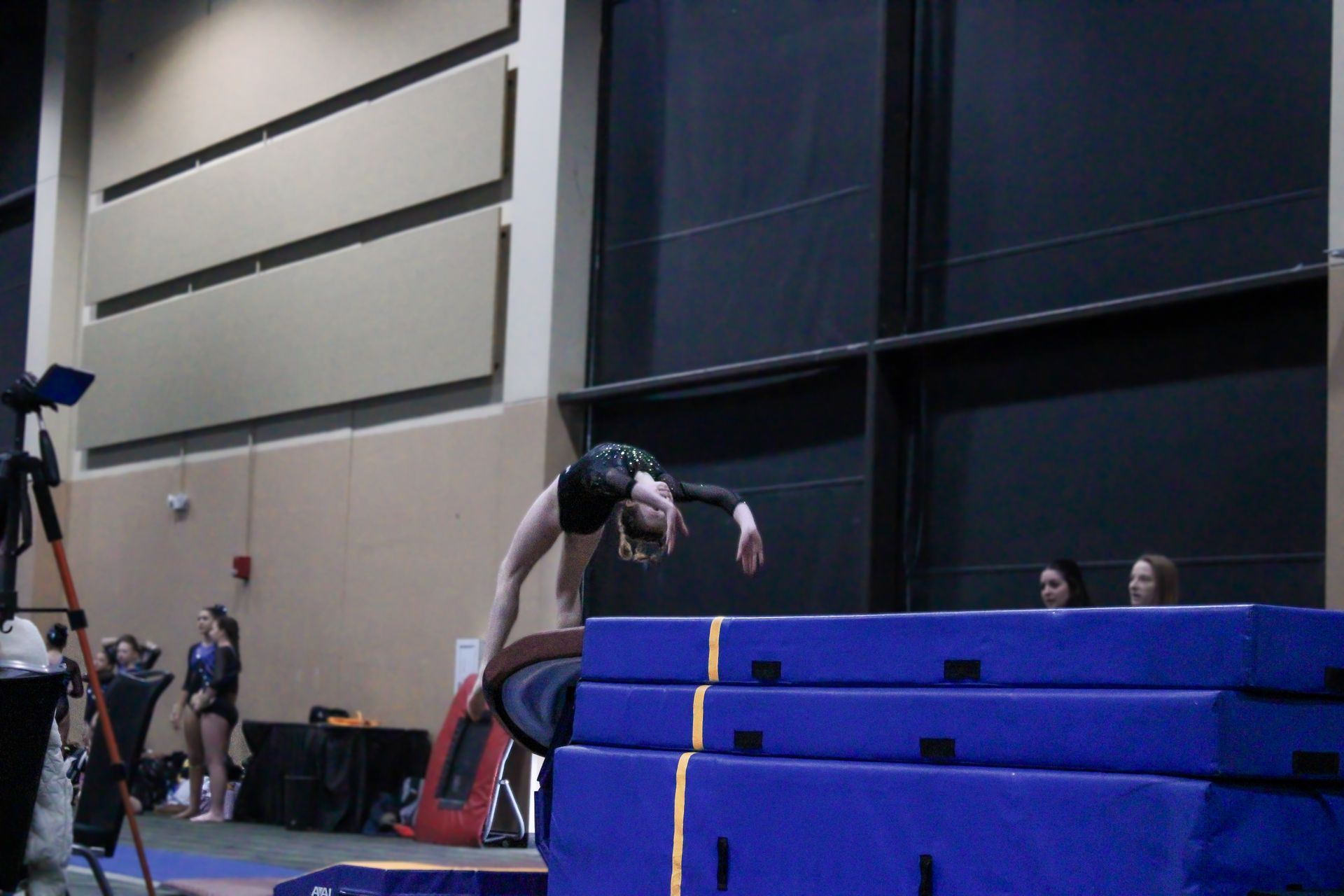 Gymnast vaulting over stacked blue mats in an indoor training gym