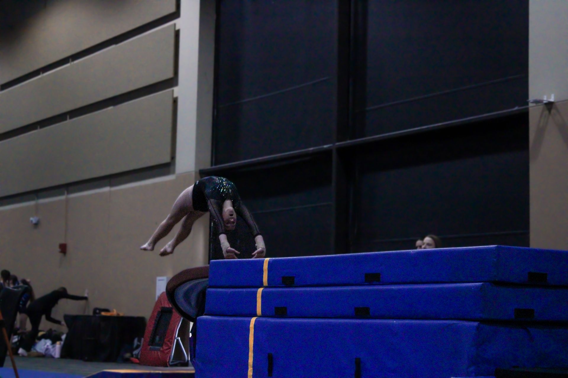 Gymnast vaulting over stacked blue mats in an indoor gymnasium