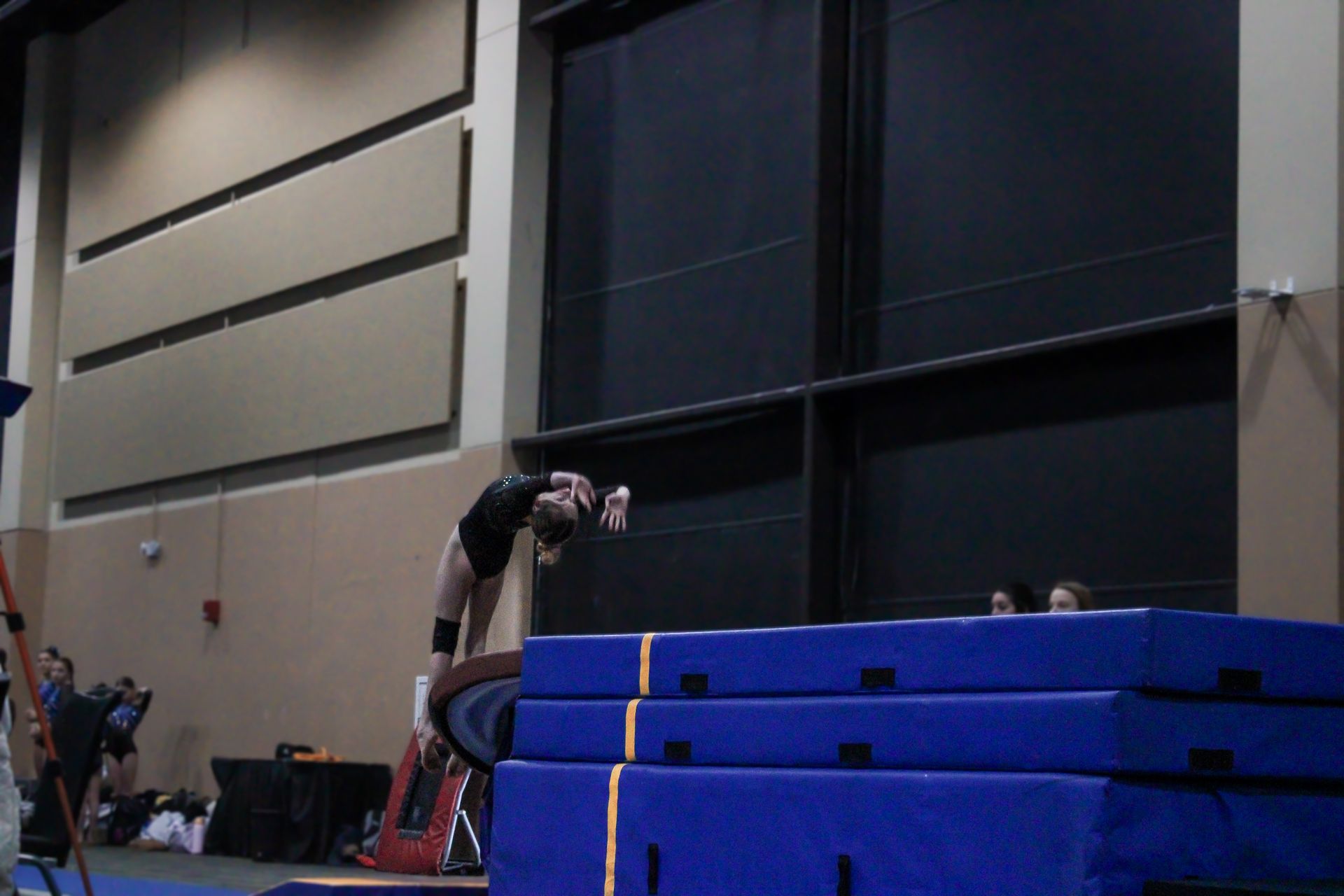 Athlete vaulting over stacked blue mats in an indoor gymnasium