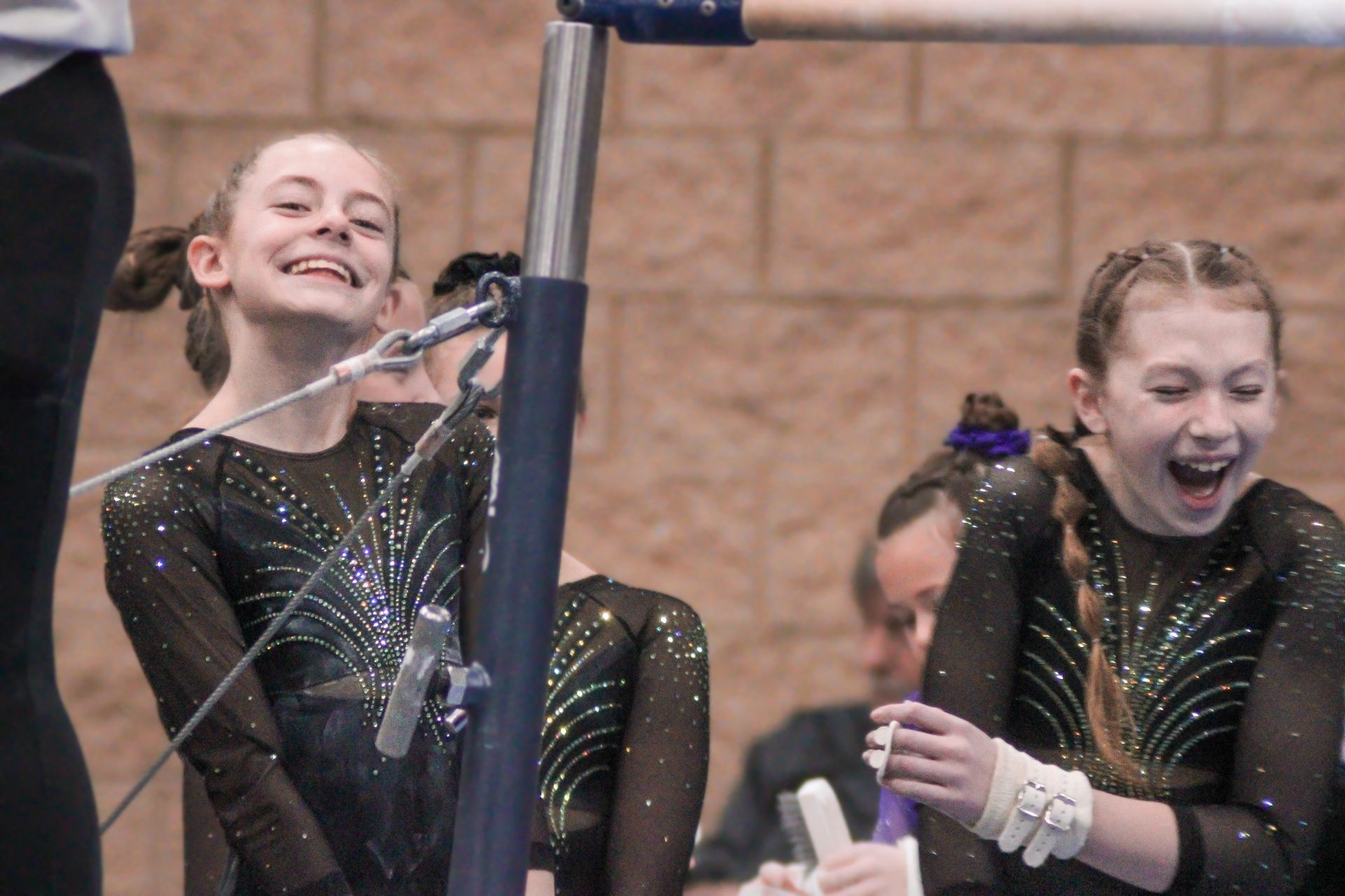 Two gymnasts in black leotards smiling during a balance beam routine