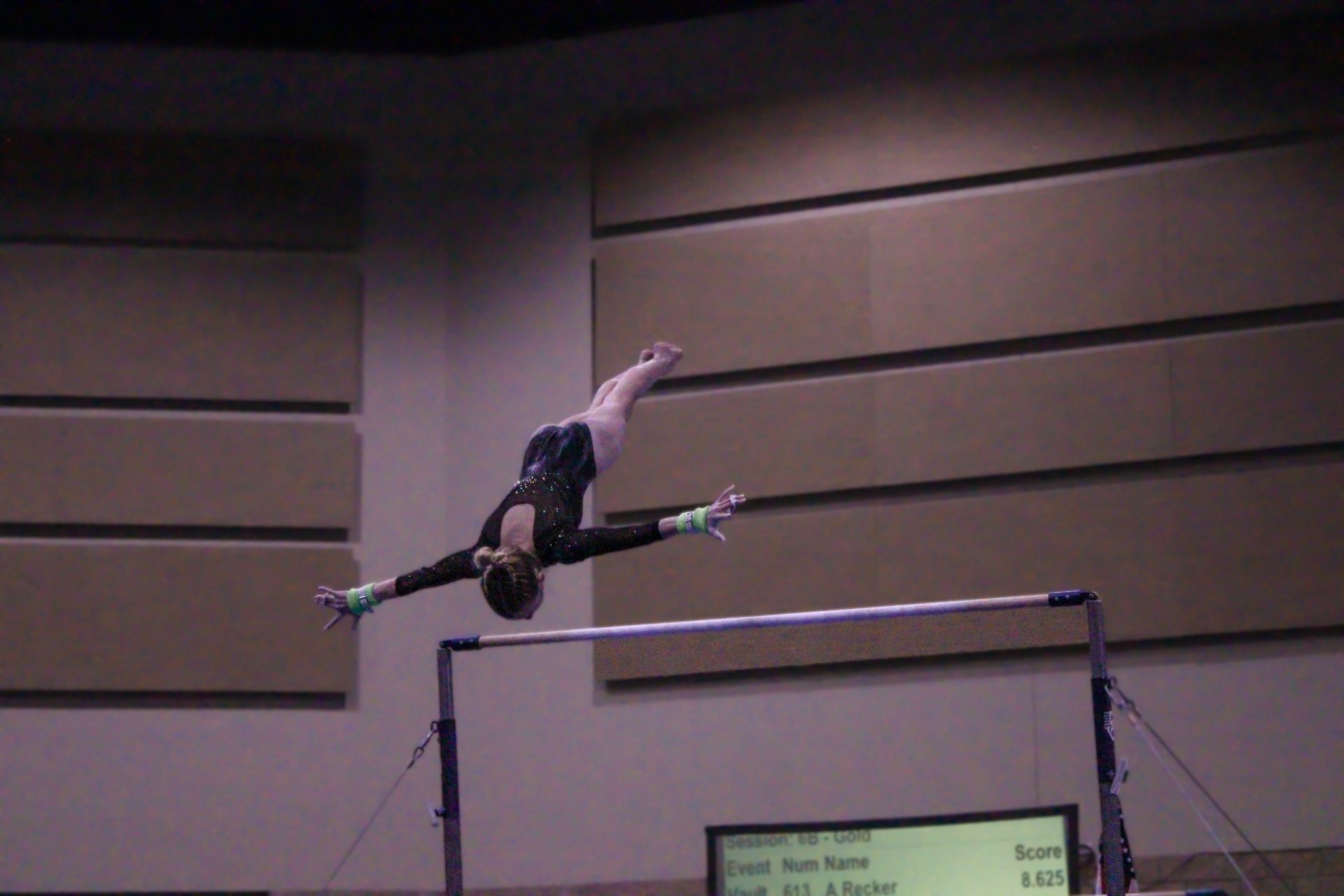 Gymnast midair above uneven bars during a routine indoors