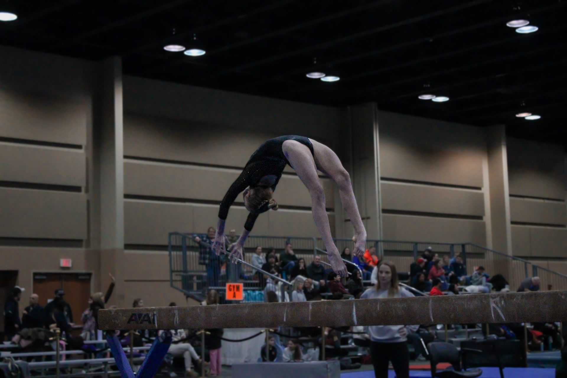 Gymnast arching backward on a balance beam during a competition in an indoor arena