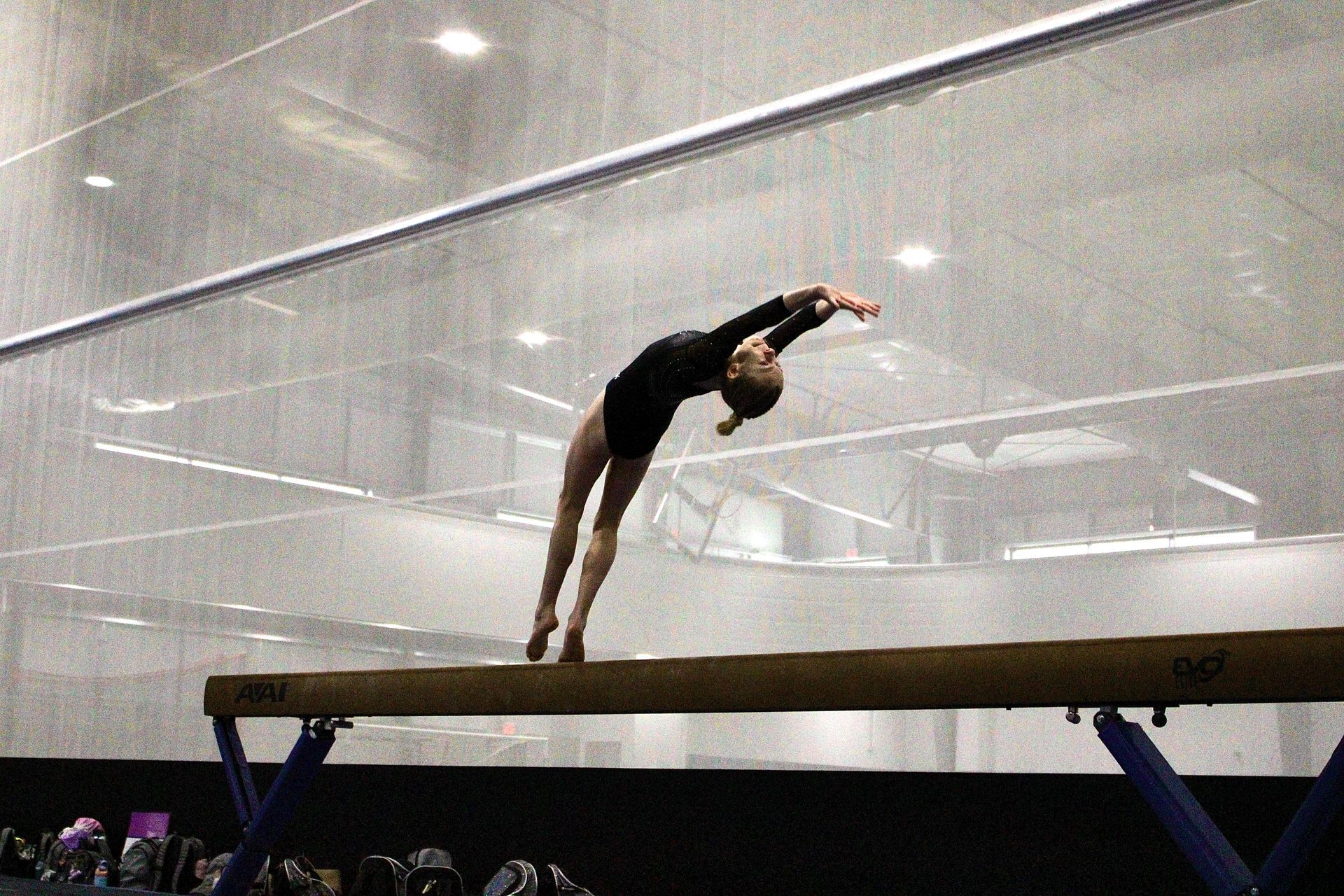 Gymnast mid-arch on a balance beam during a routine in a bright indoor arena