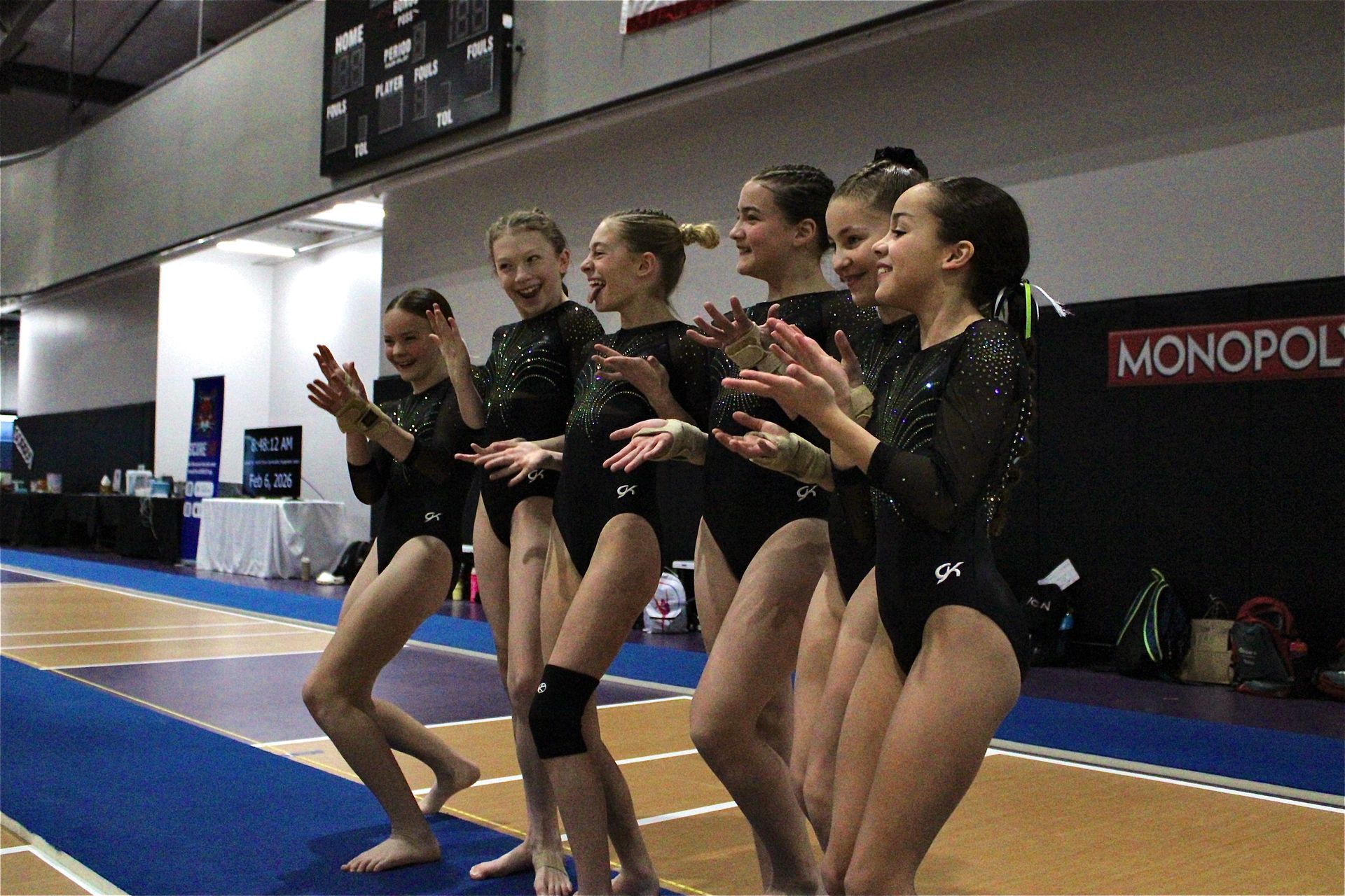 Gymnasts in black leotards posing on a blue mat during a floor routine warm-up indoors