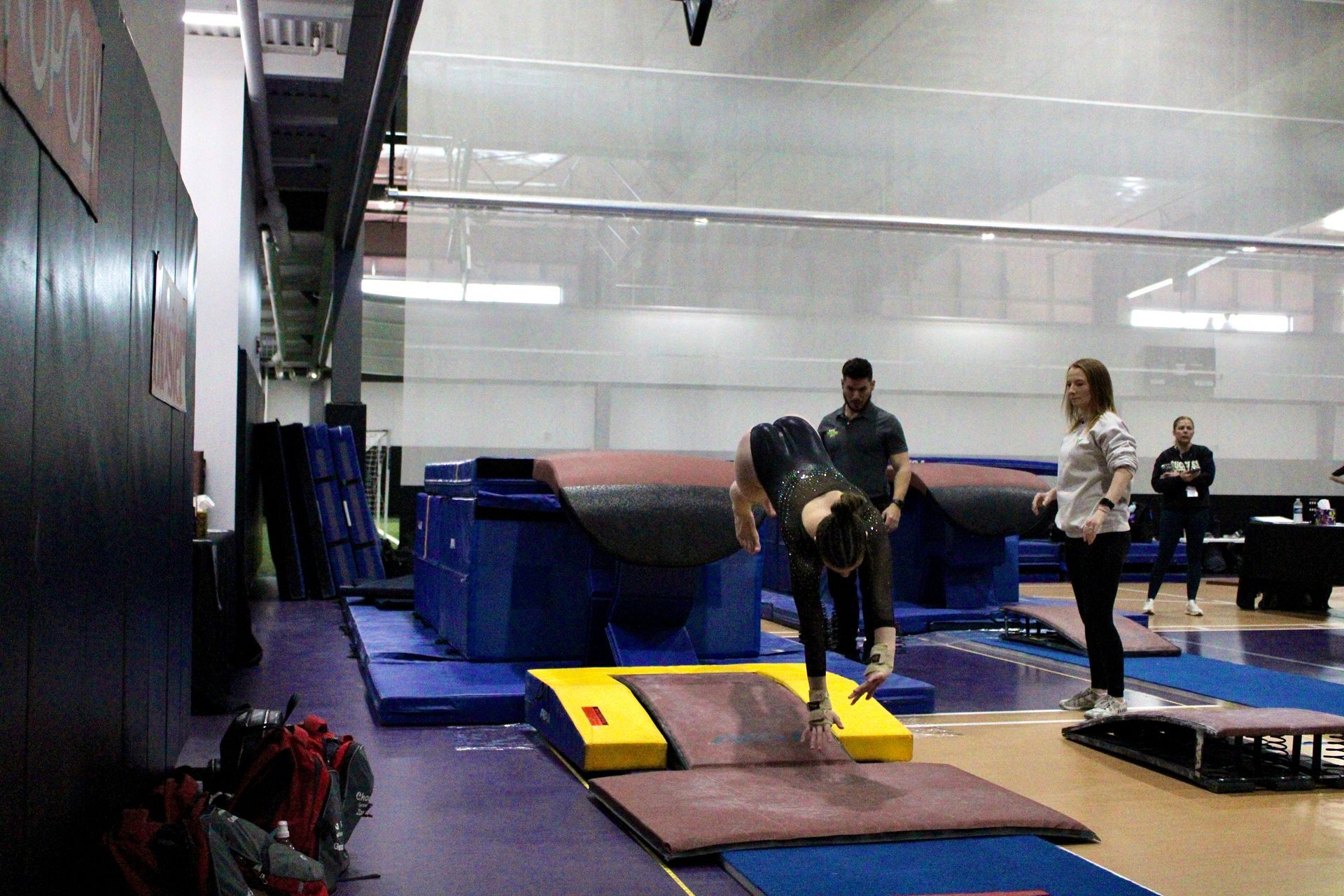 Gymnastics training area with people practicing vaults and mats indoors