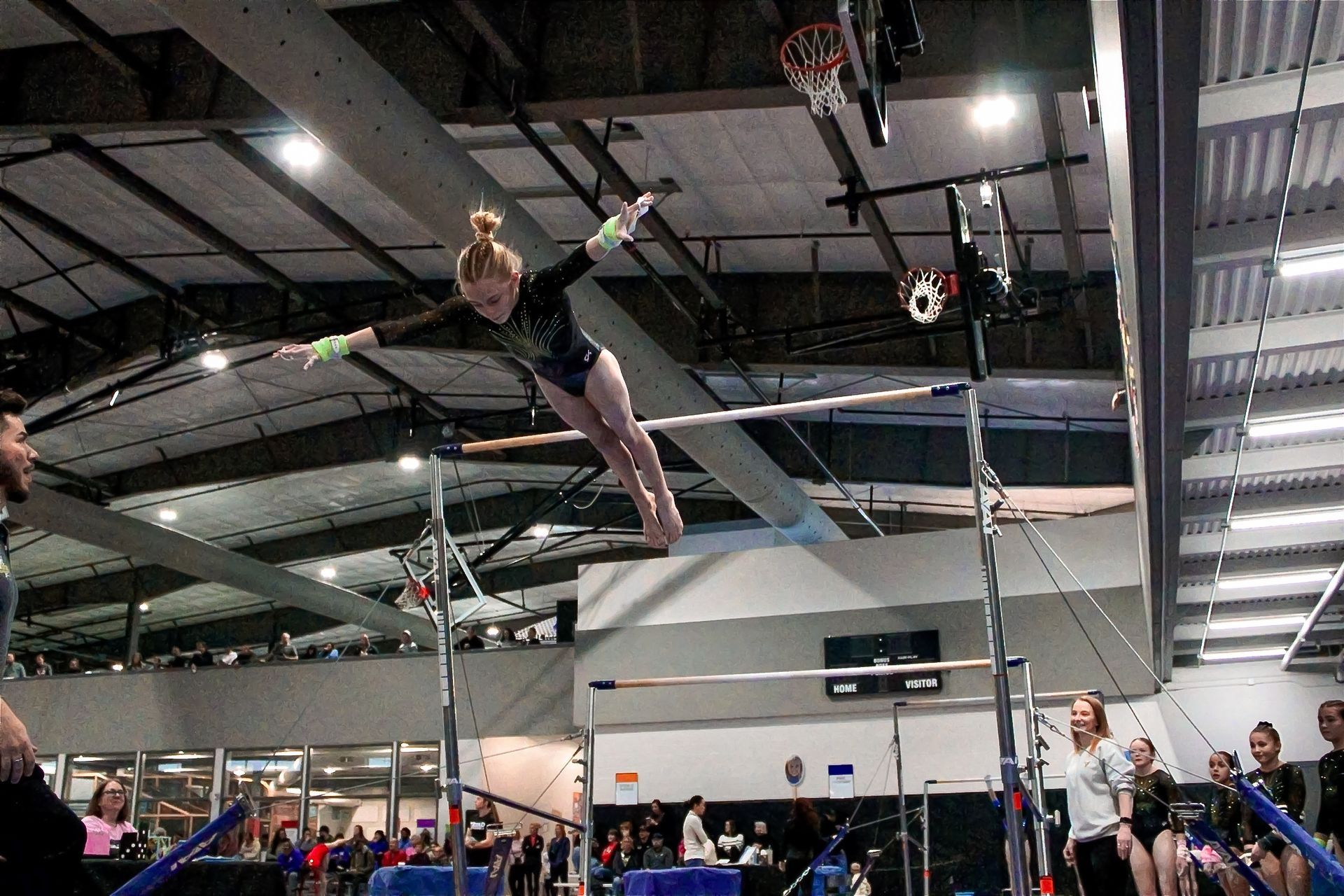 Pole vaulter clearing the bar indoors at a track meet, with spectators watching.