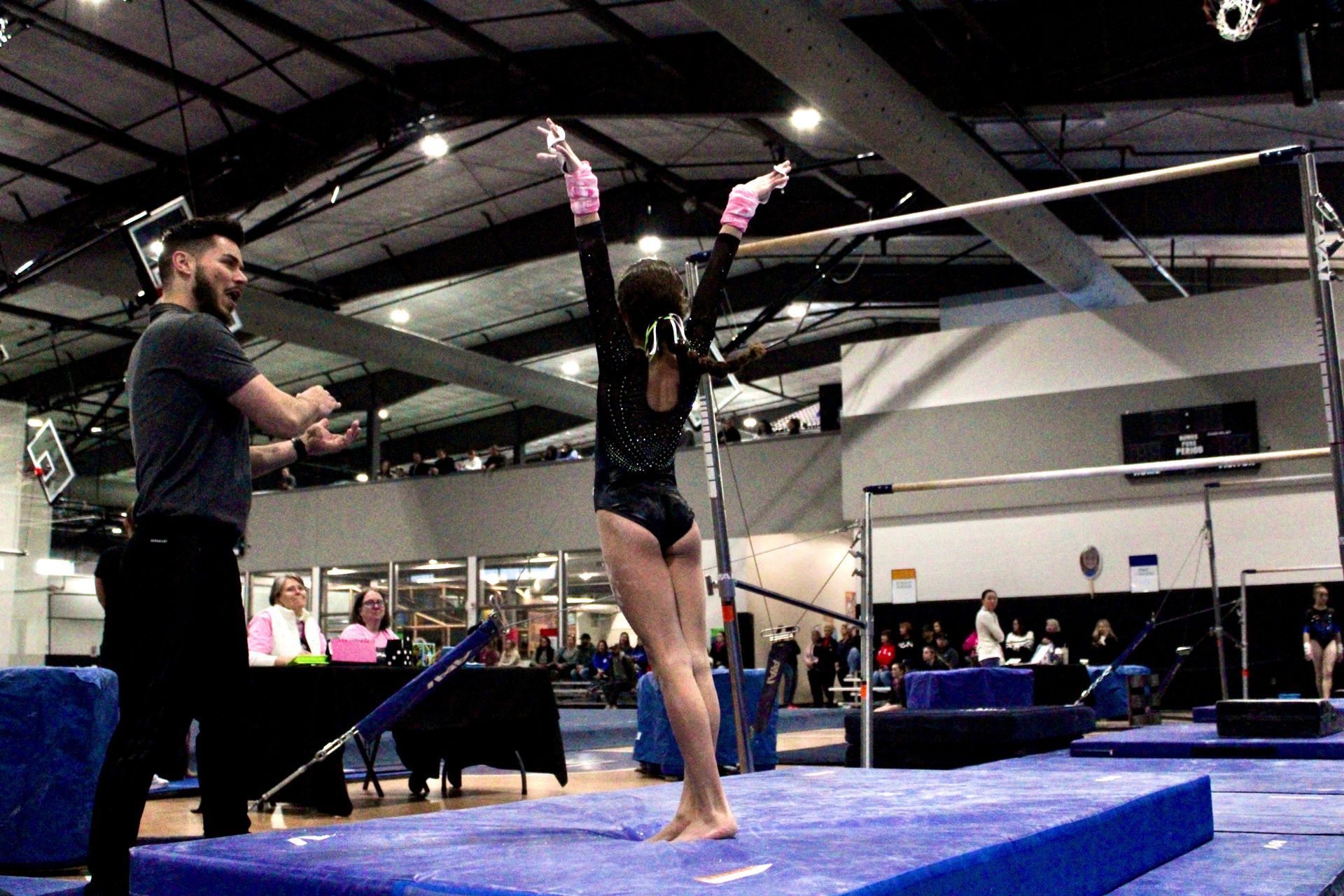 Gymnast balancing on beam in a gymnasium, with a coach watching nearby