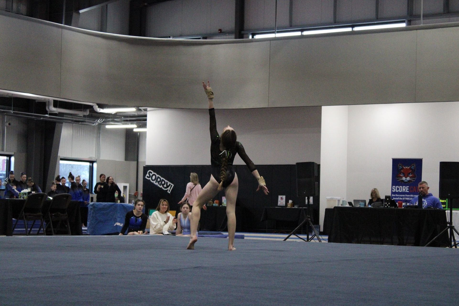 Gymnast performing an inverted pose on a blue mat in an indoor competition hall