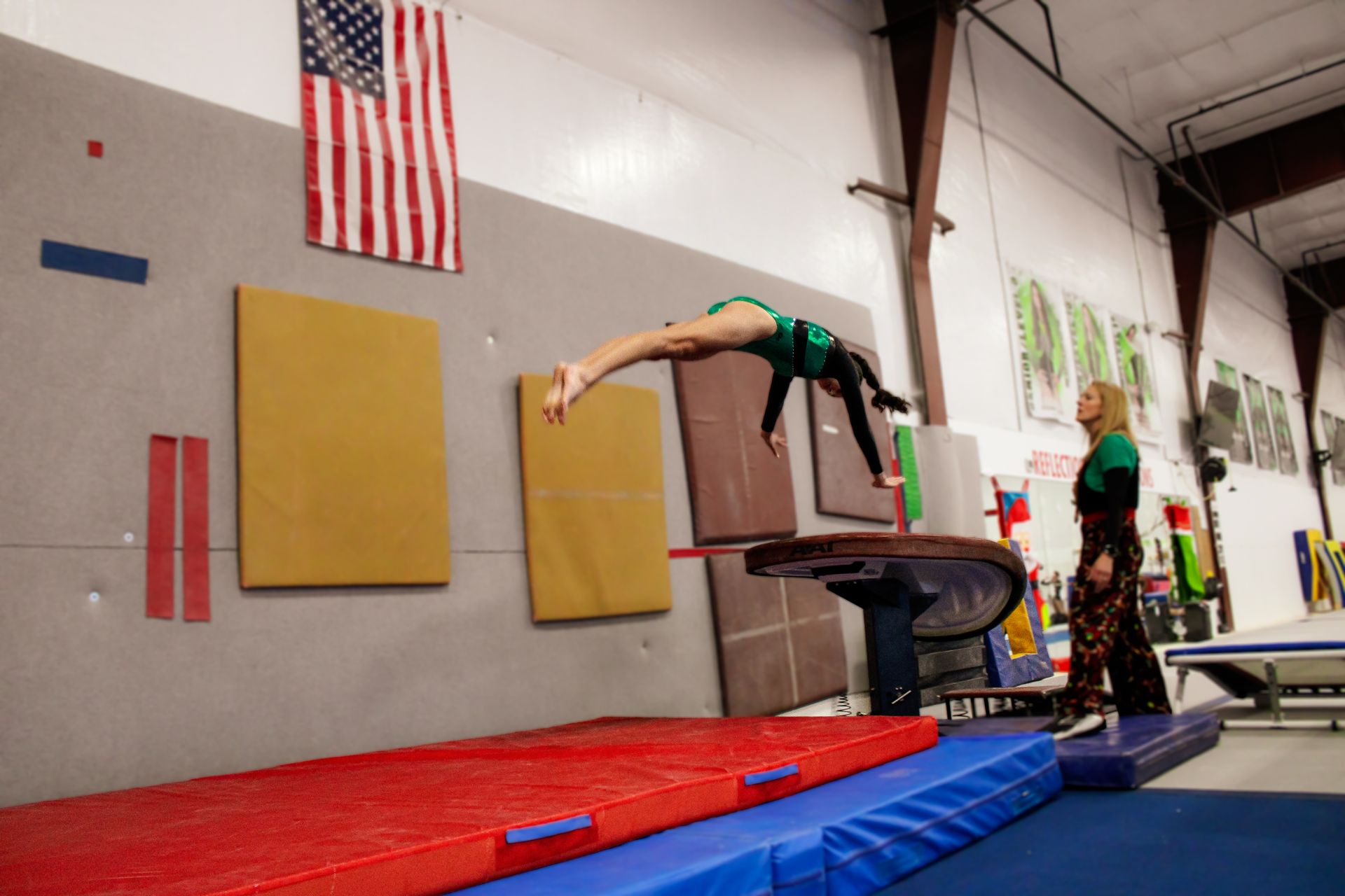 Gymnast performing a back arch over a vault in a gymnastics gym with red and blue mats