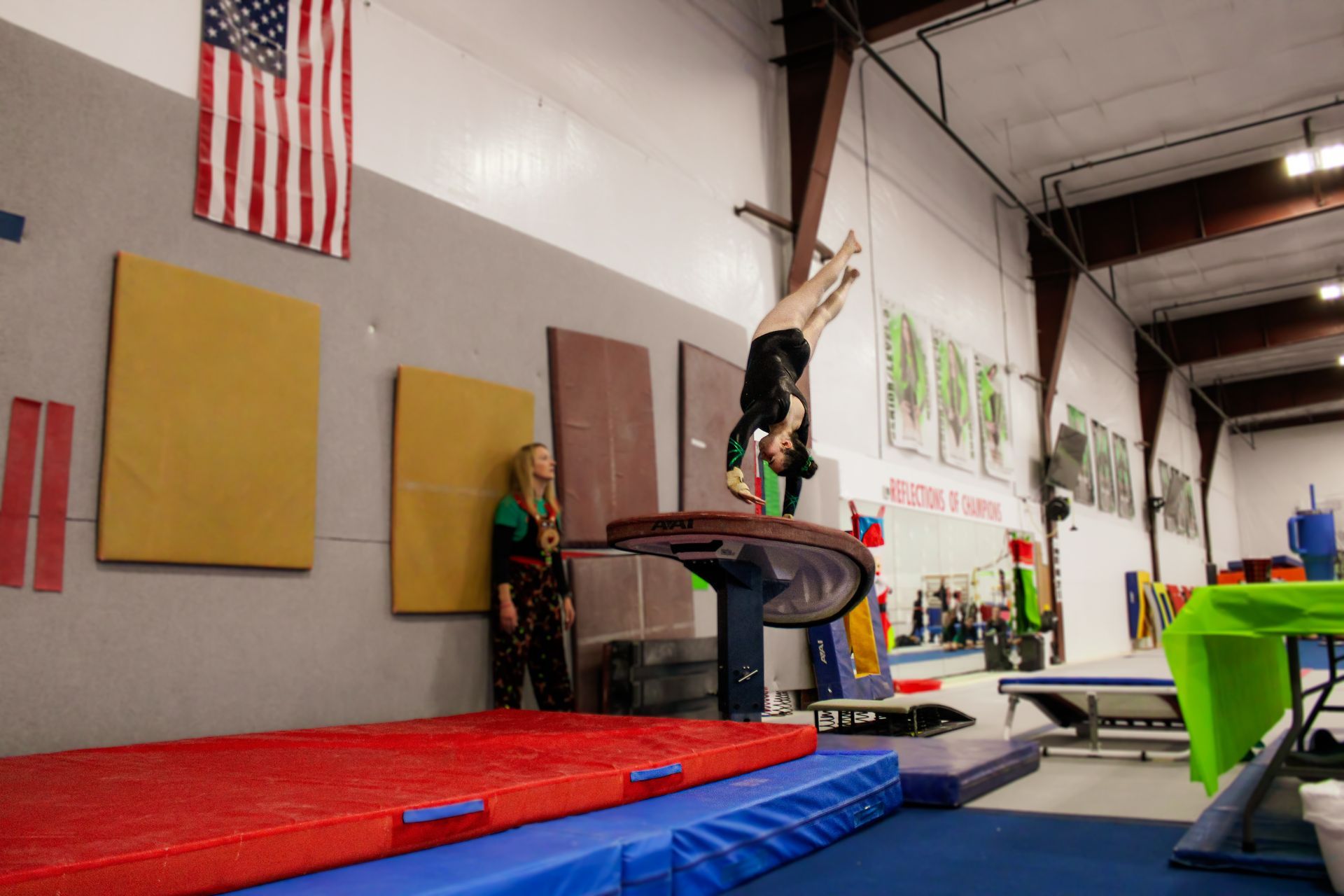 Gymnast on balance beam in an indoor gym with red and blue mats