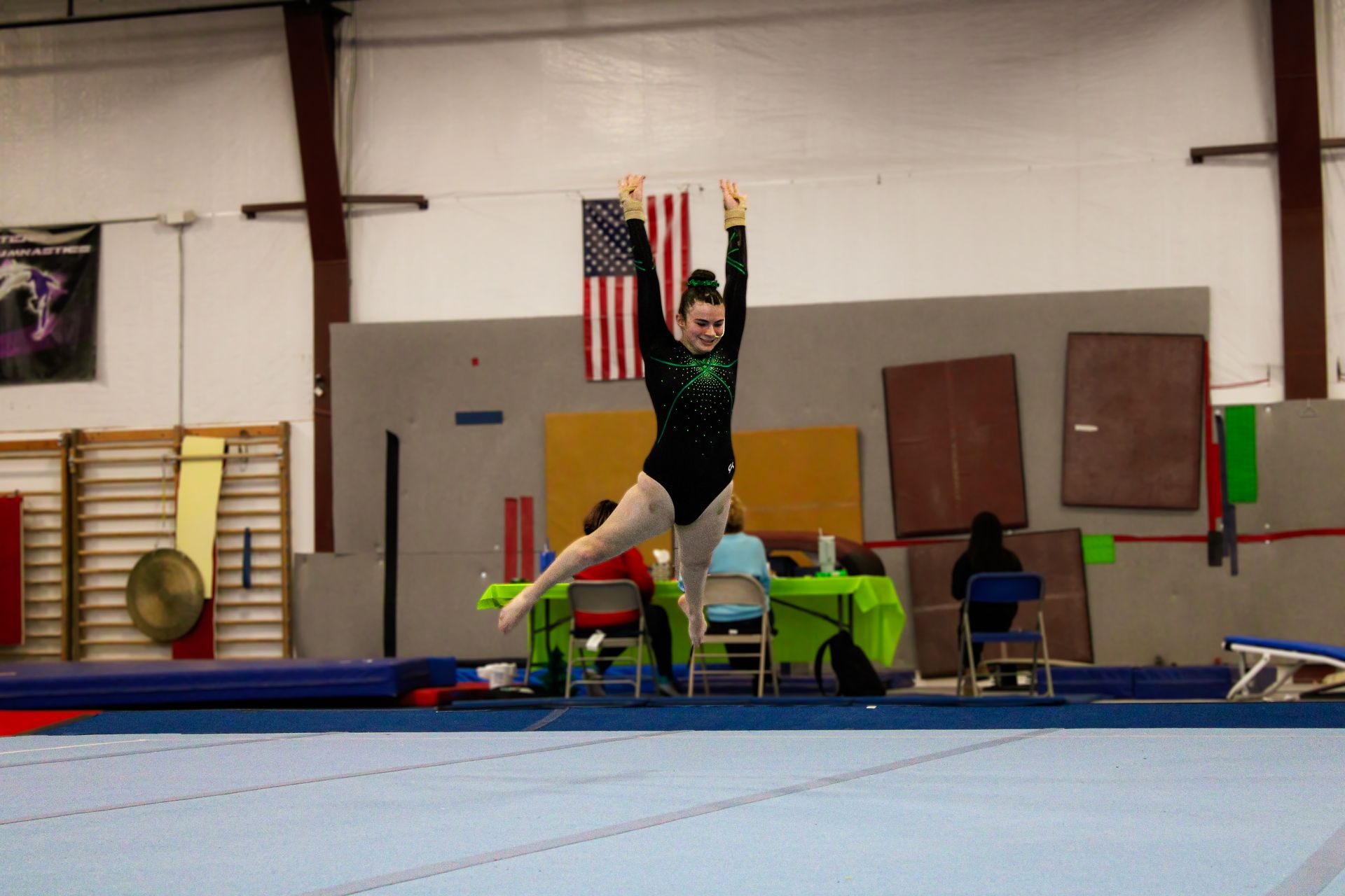Gymnast midair on a trampoline in an indoor gym, arms raised above head