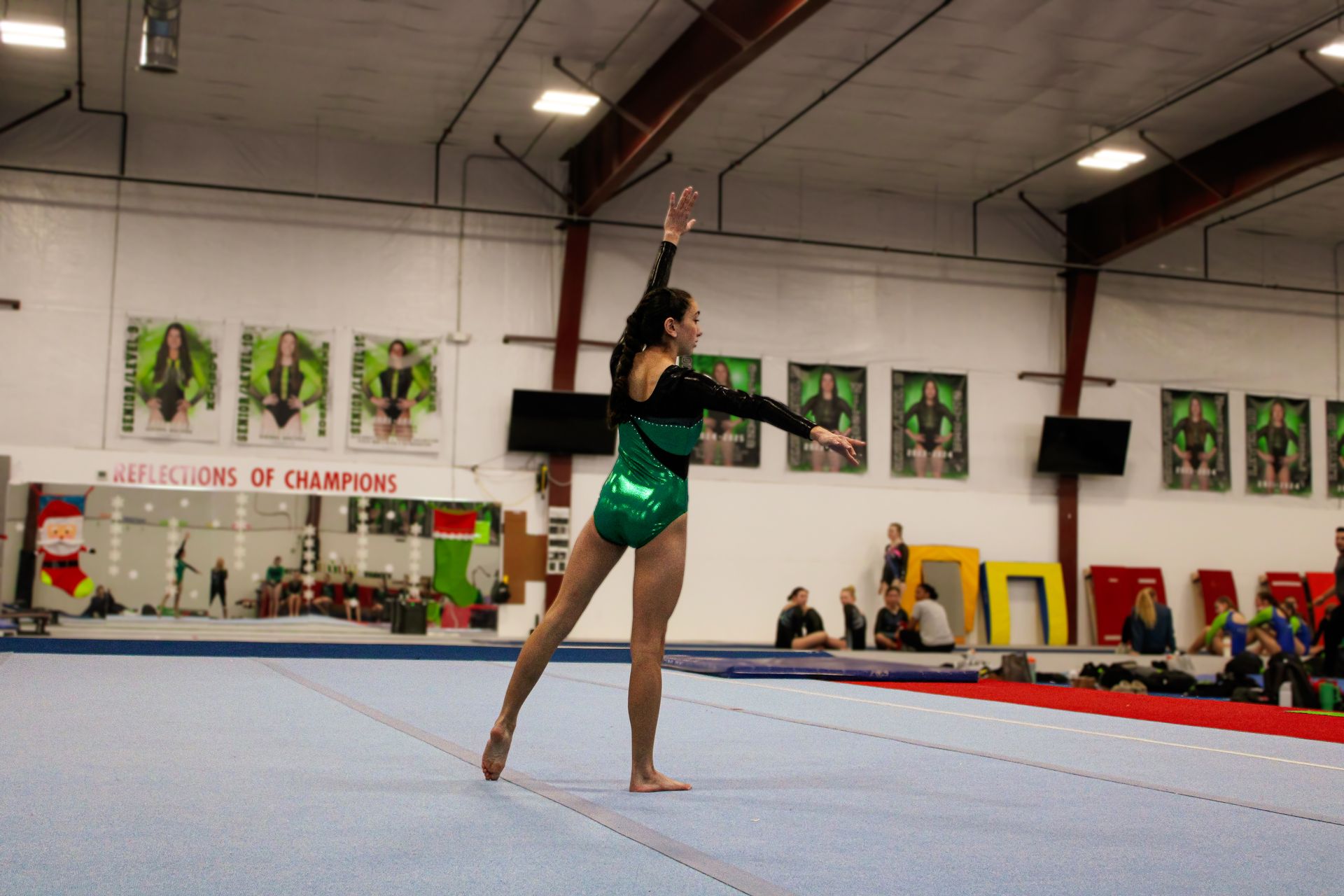 Gymnast in a green leotard posing on a gymnastics floor in an indoor gymnasium.